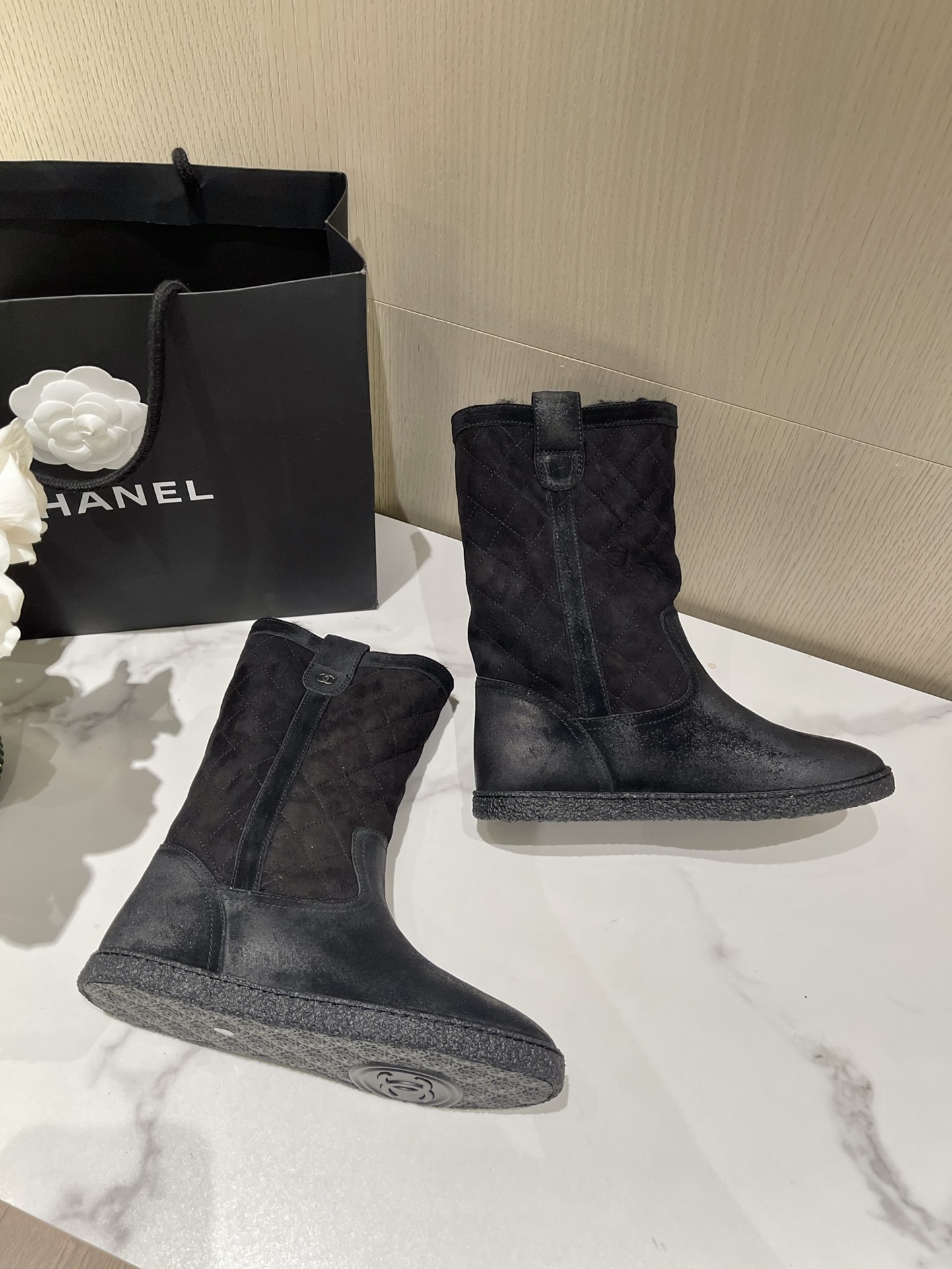 A pair of black Chanel quilted suede winter boots with fur lining and silver CC logo detail on a marble tabletop. - Hình 5