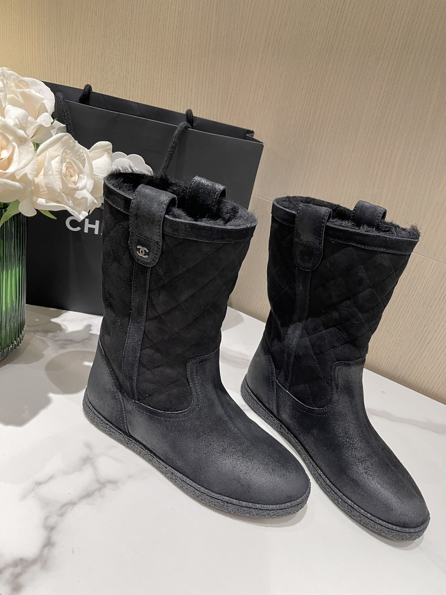 A pair of black Chanel quilted suede winter boots with fur lining and silver CC logo detail on a marble tabletop. - Hình 4