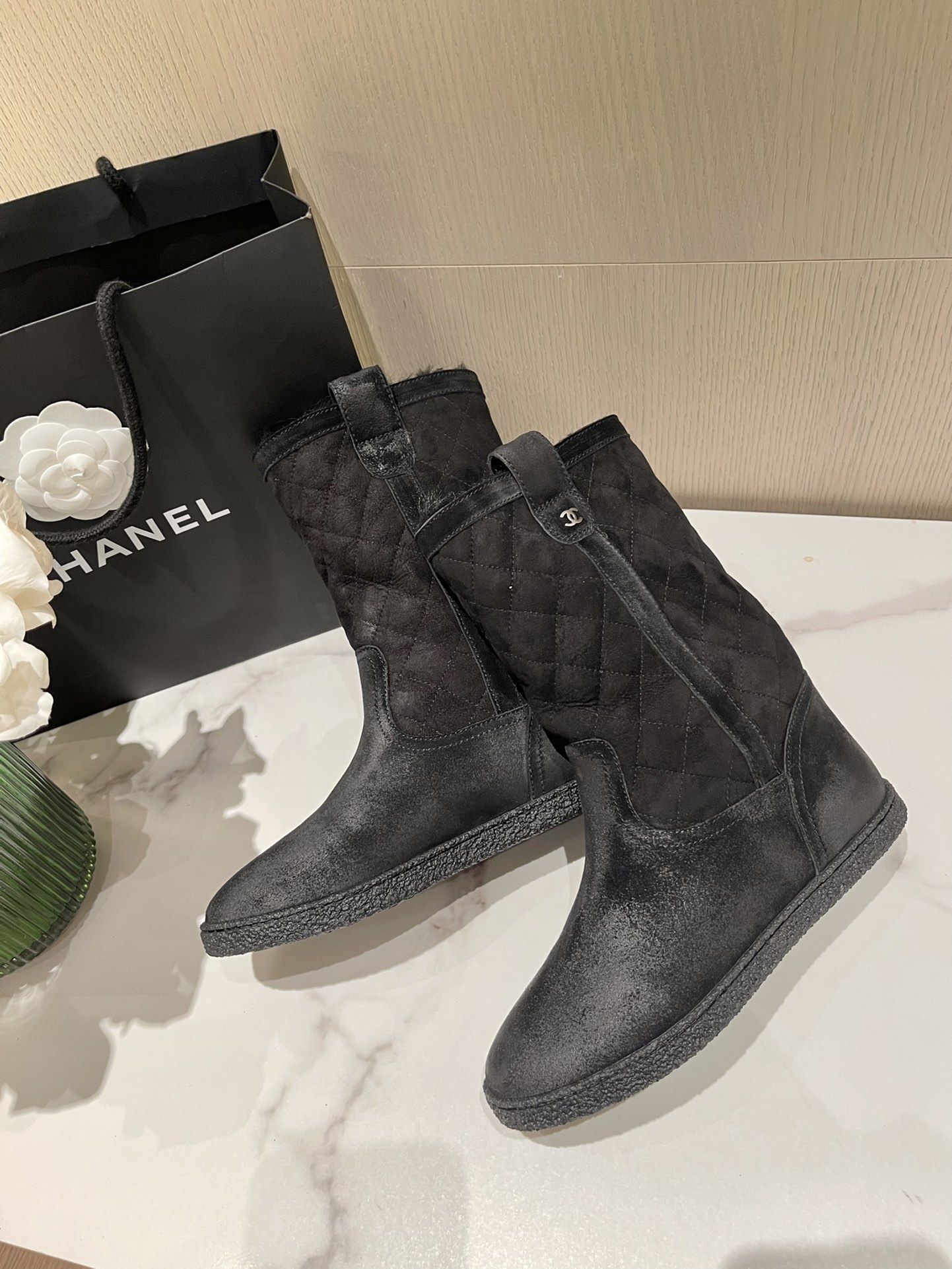 A pair of black Chanel quilted suede winter boots with fur lining and silver CC logo detail on a marble tabletop. - Hình 3