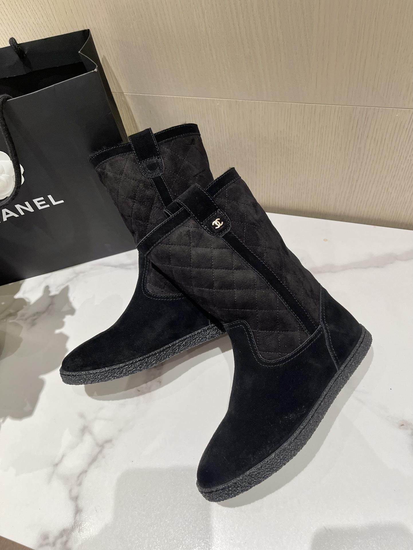 Pair of Chanel black quilted suede mid-calf winter boots with fur lining and gold CC logo displayed on a marble surface. - Hình 4