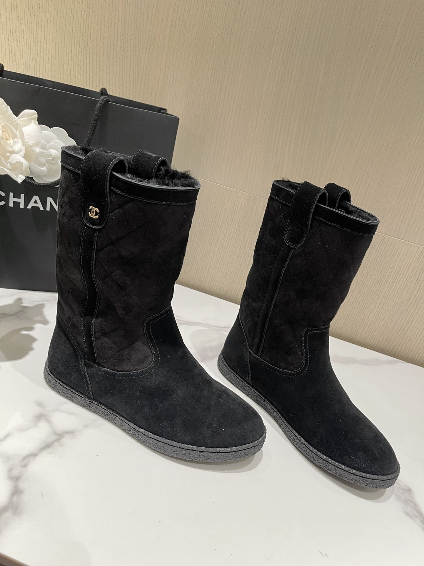 Pair of Chanel black quilted suede mid-calf winter boots with fur lining and gold CC logo displayed on a marble surface. - Hình 3