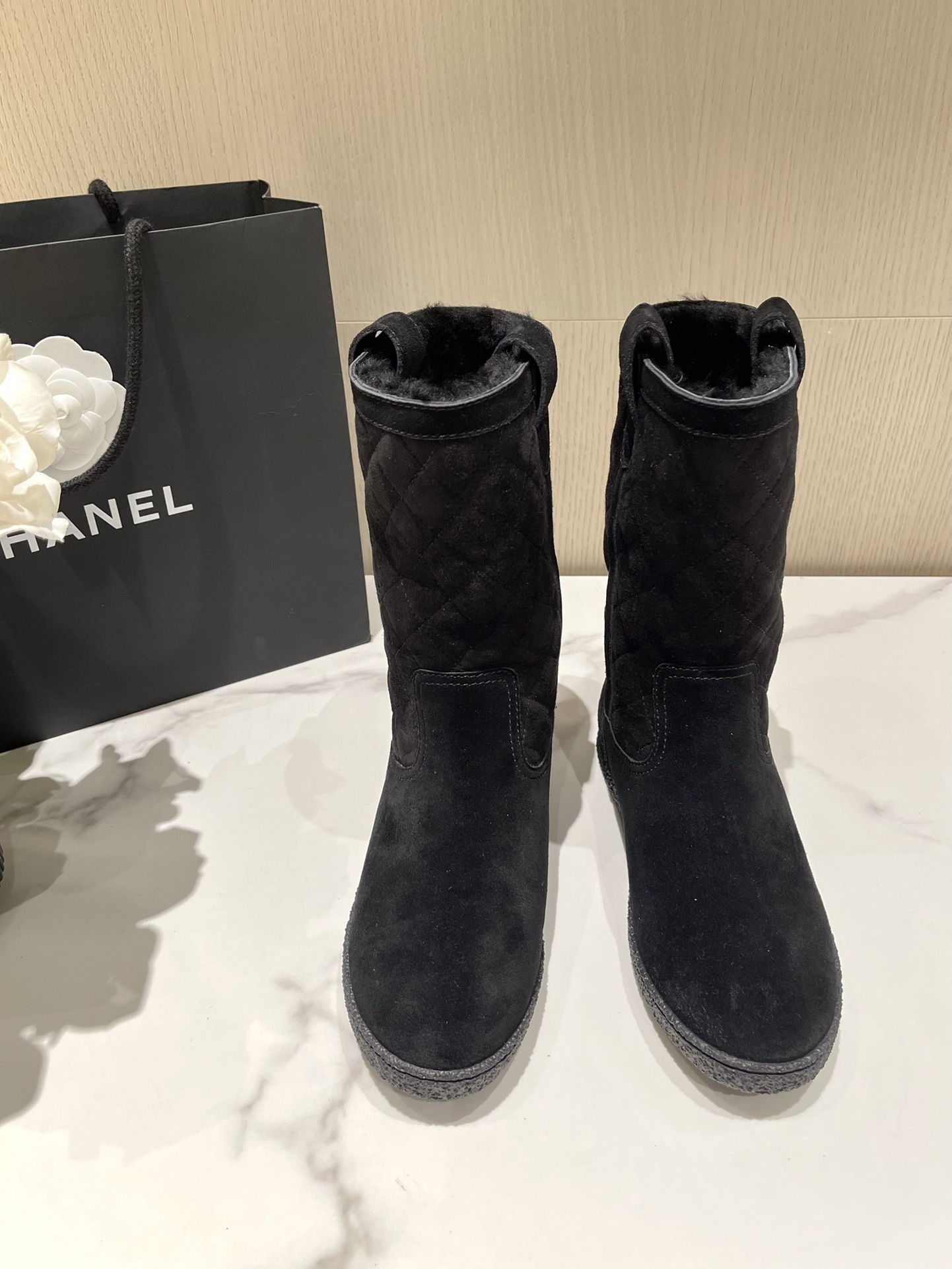 Pair of Chanel black quilted suede mid-calf winter boots with fur lining and gold CC logo displayed on a marble surface. - Hình 2