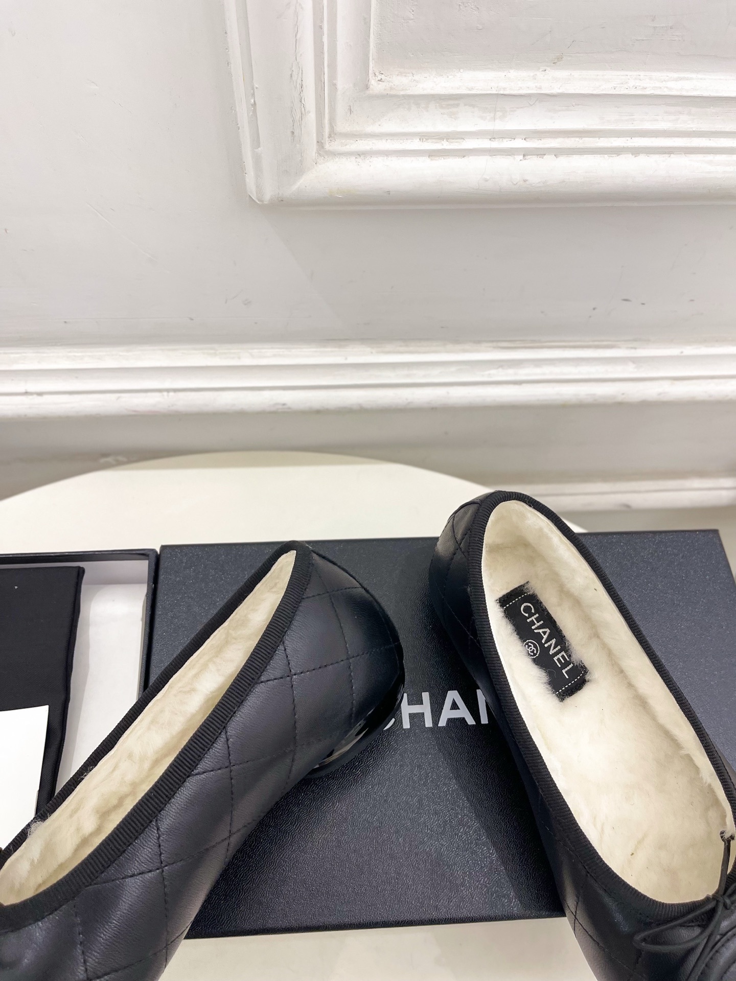 Pair of black Chanel quilted leather ballet flats with white fur lining and CC logo on a table - Hình 8
