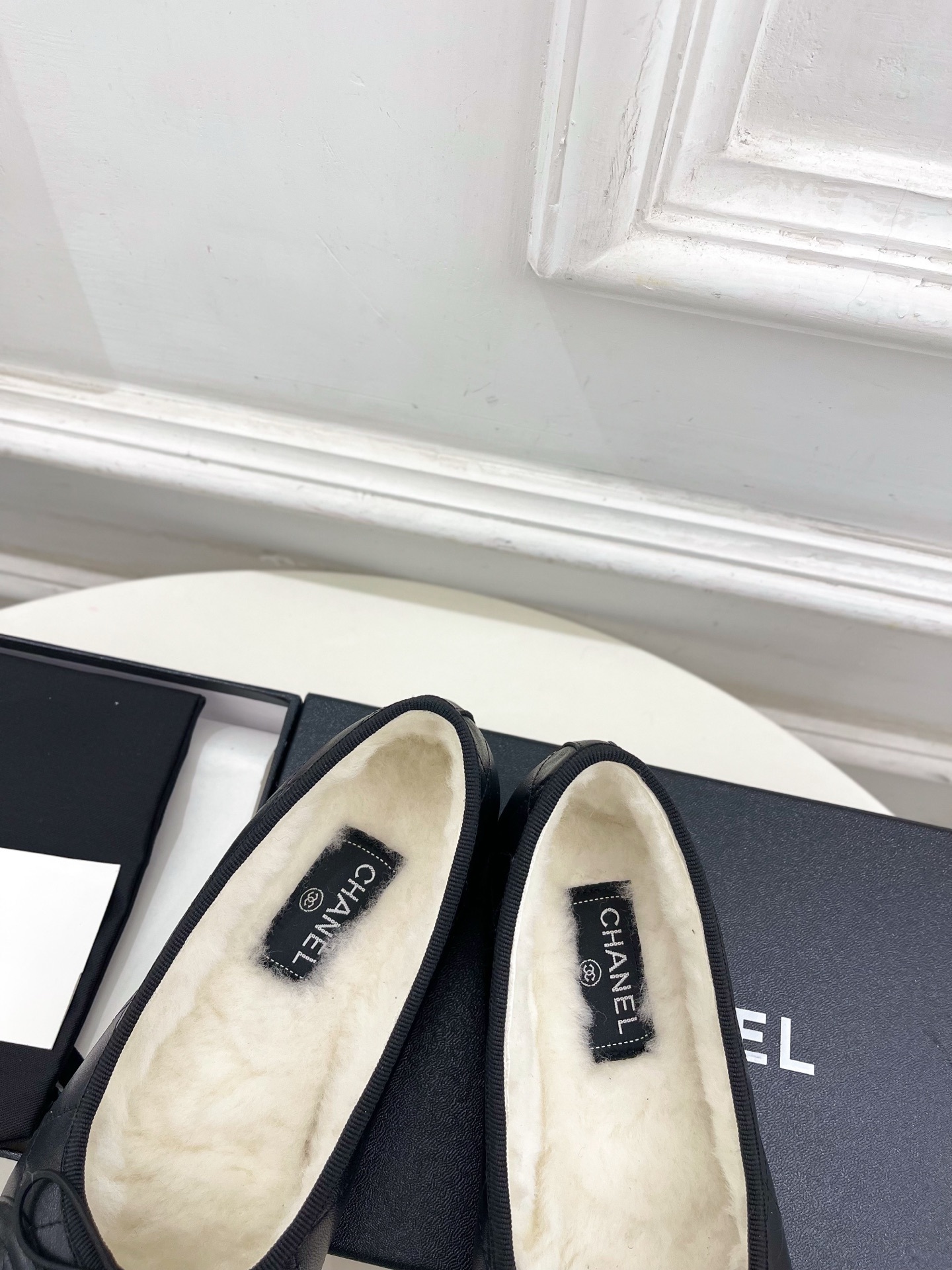 Pair of black Chanel quilted leather ballet flats with white fur lining and CC logo on a table - Hình 7