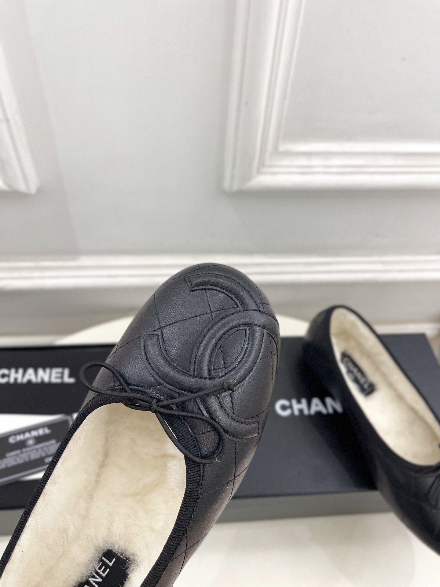 Pair of black Chanel quilted leather ballet flats with white fur lining and CC logo on a table - Hình 6