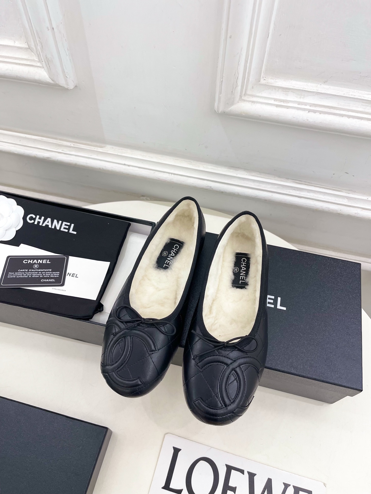 Pair of black Chanel quilted leather ballet flats with white fur lining and CC logo on a table - Hình 5