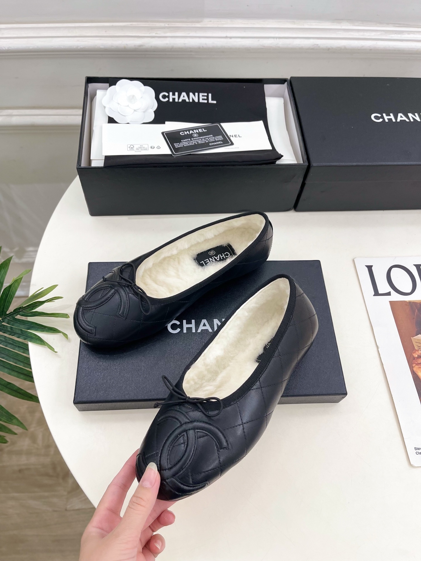 Pair of black Chanel quilted leather ballet flats with white fur lining and CC logo on a table - Hình 3