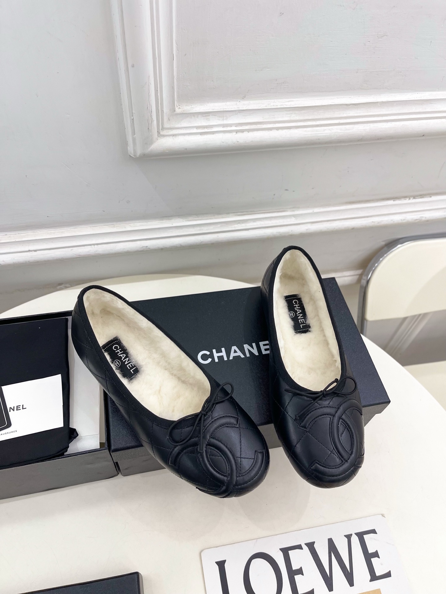 Pair of black Chanel quilted leather ballet flats with white fur lining and CC logo on a table - Hình 2