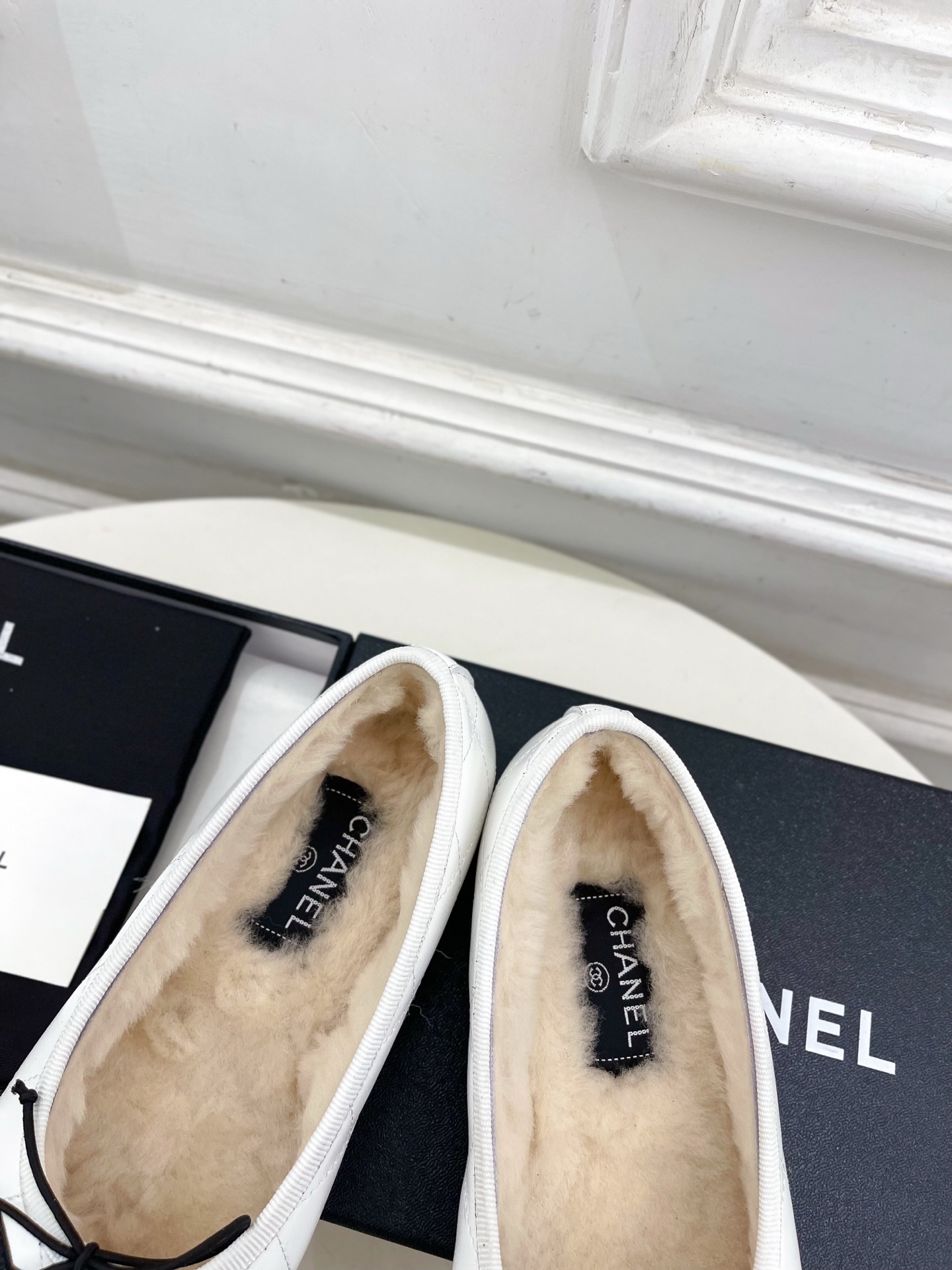 Pair of Chanel white quilted leather ballet flats with black CC logo and shearling lining on a display table. - Hình 8