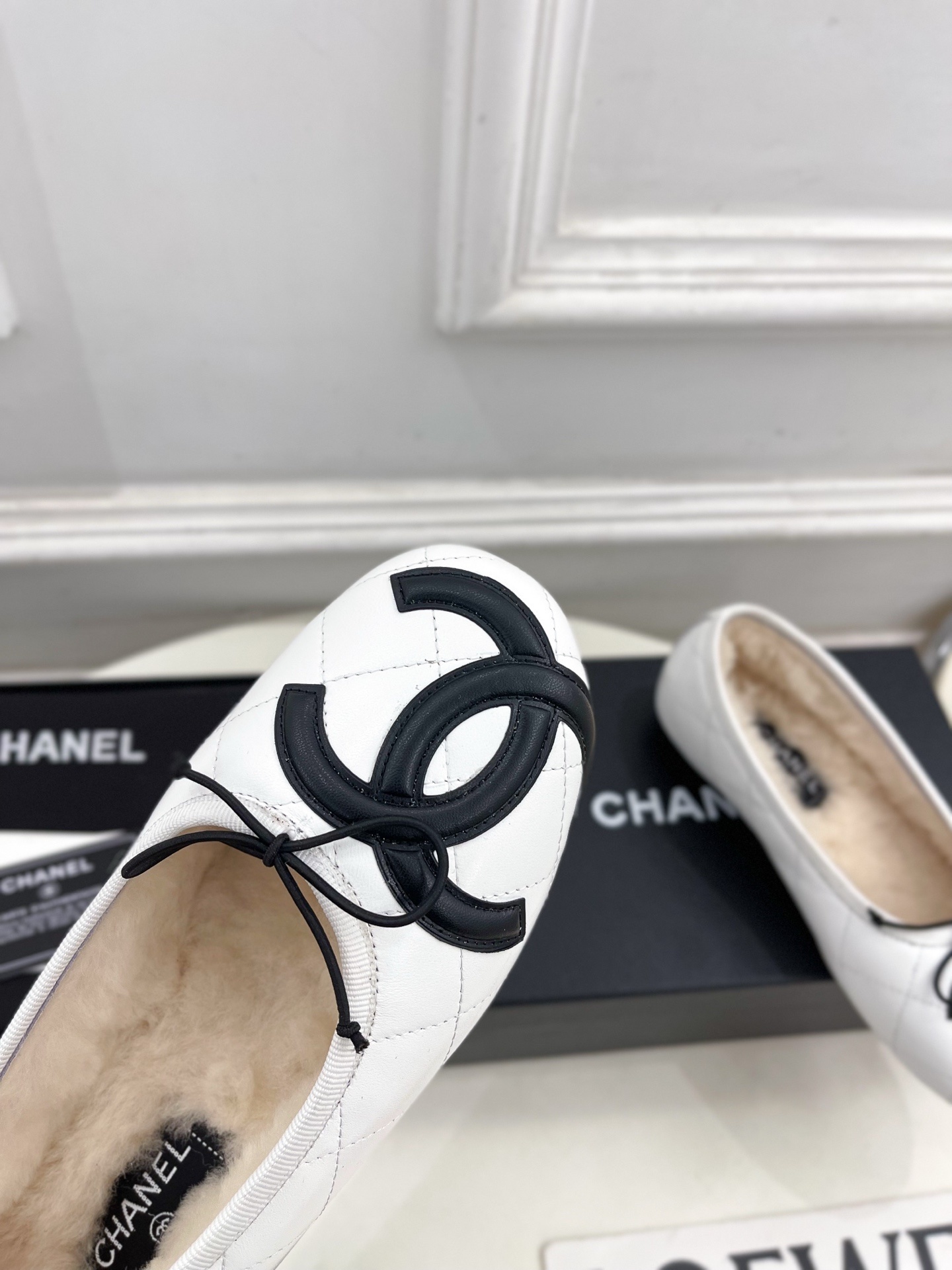 Pair of Chanel white quilted leather ballet flats with black CC logo and shearling lining on a display table. - Hình 6