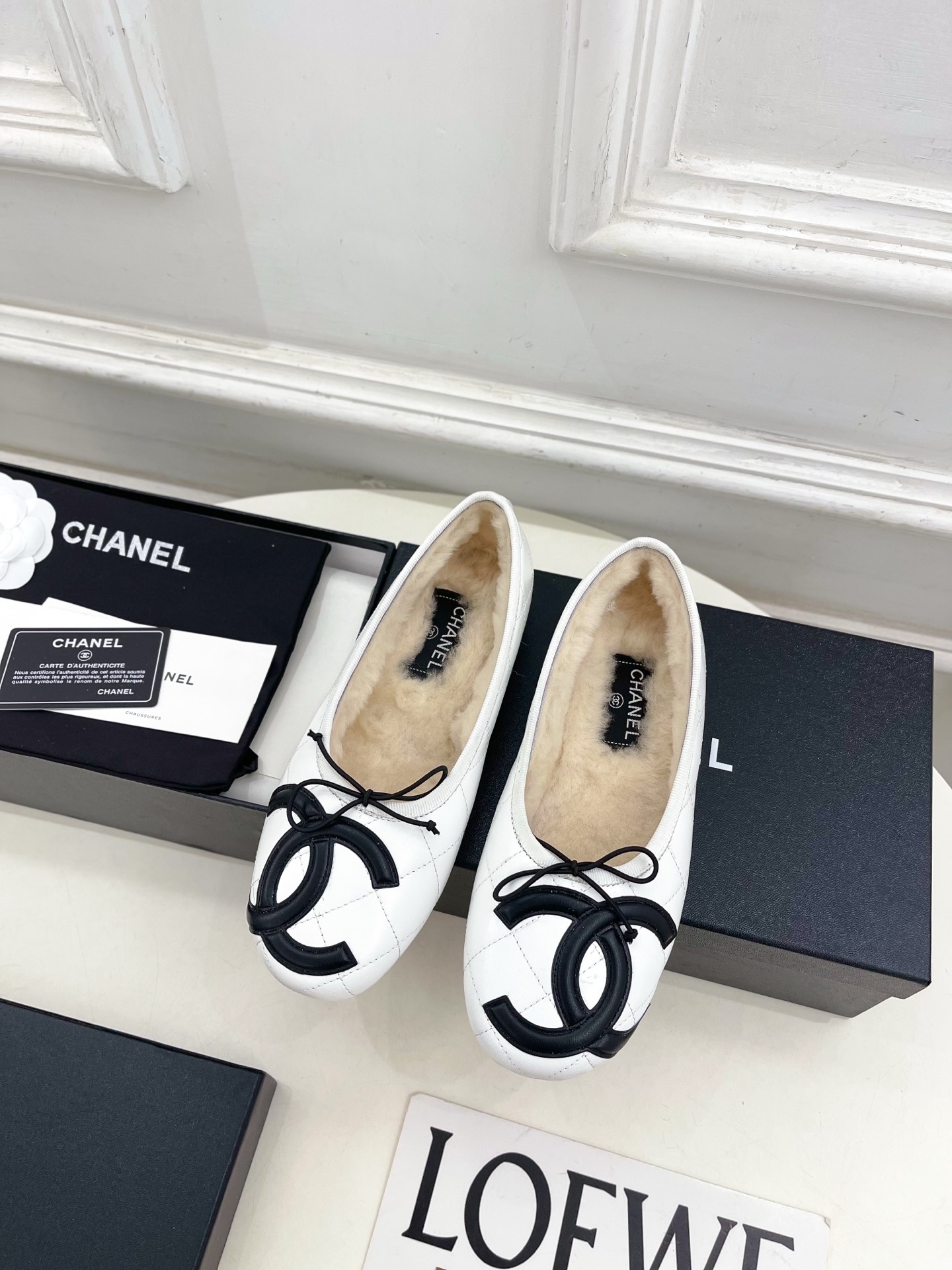 Pair of Chanel white quilted leather ballet flats with black CC logo and shearling lining on a display table. - Hình 5