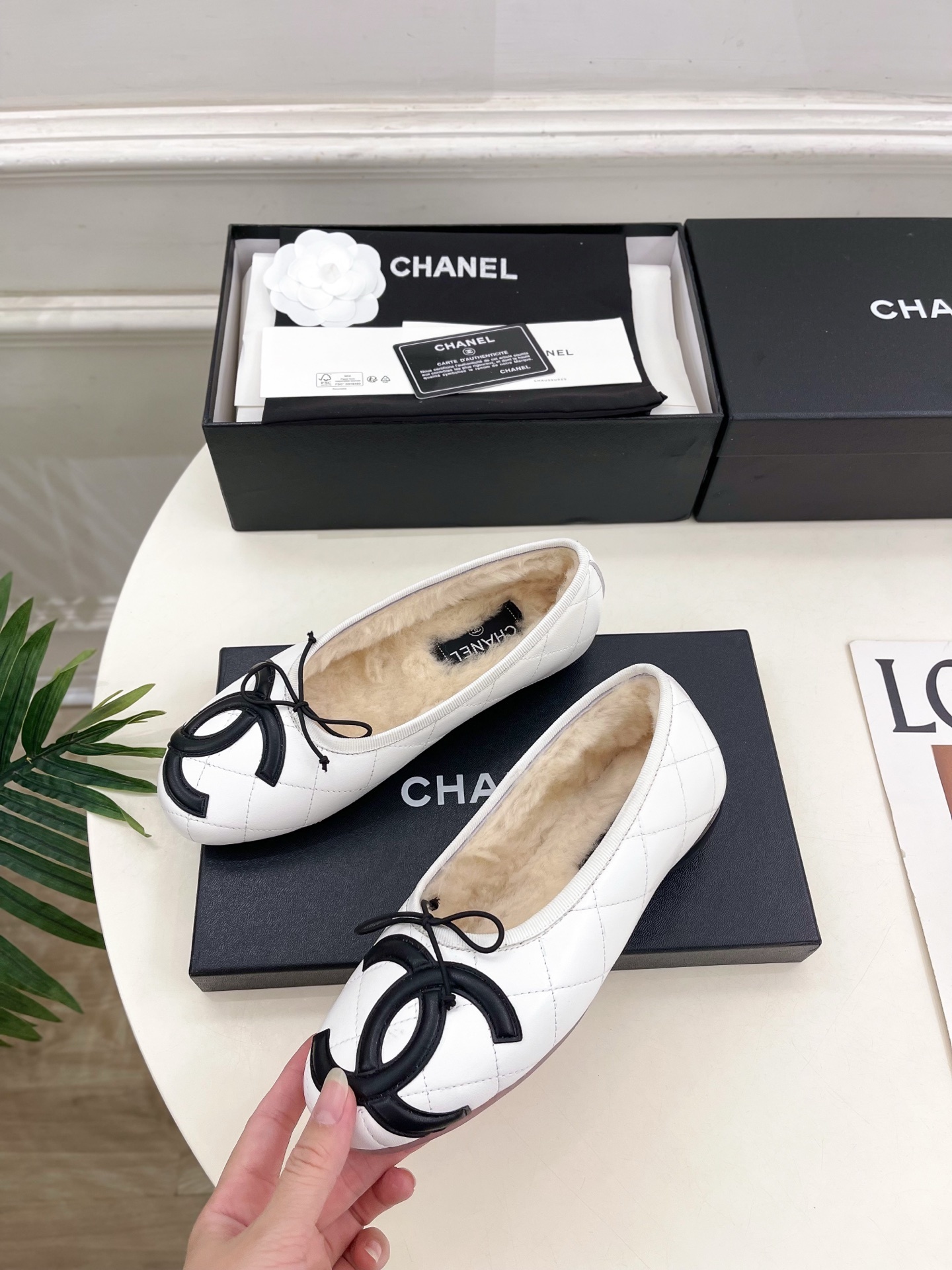 Pair of Chanel white quilted leather ballet flats with black CC logo and shearling lining on a display table. - Hình 3