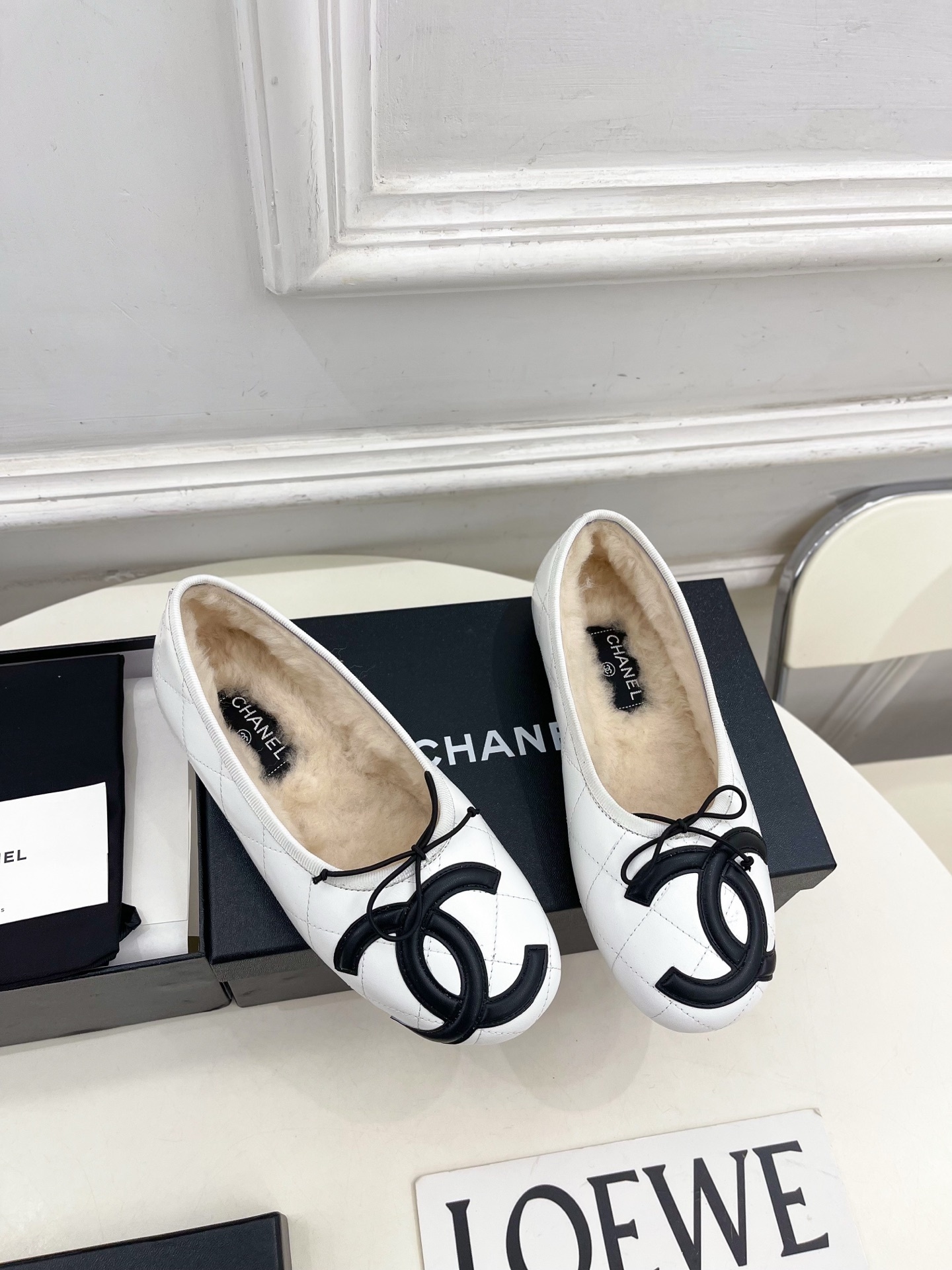 Pair of Chanel white quilted leather ballet flats with black CC logo and shearling lining on a display table. - Hình 2