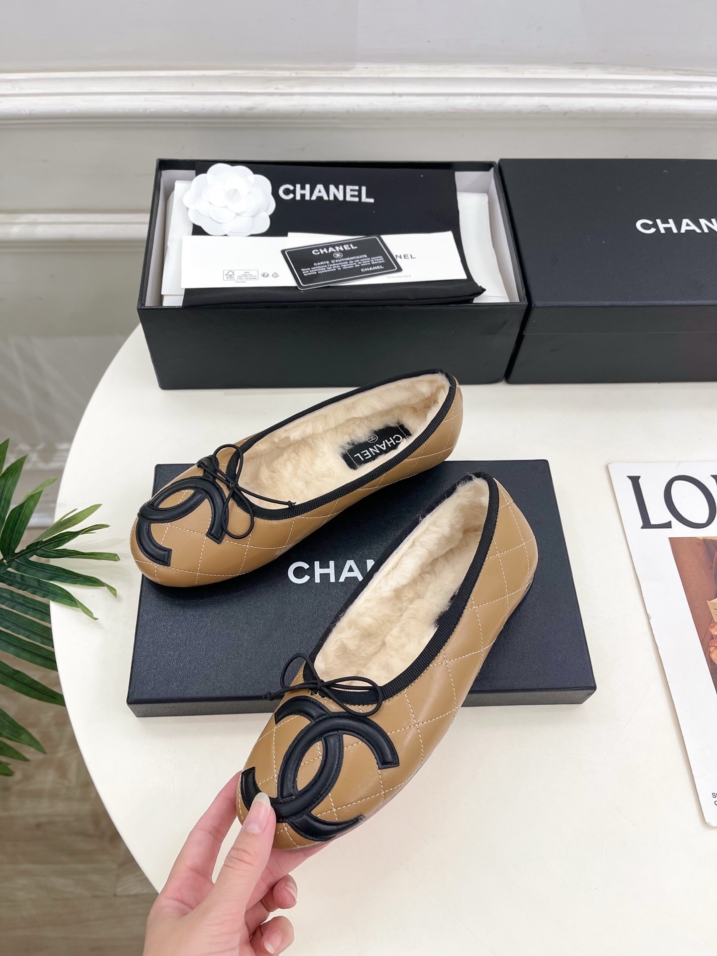 Pair of tan Chanel quilted ballerina flats with black CC logo and fuzzy shearling lining on a white table. - Hình 3