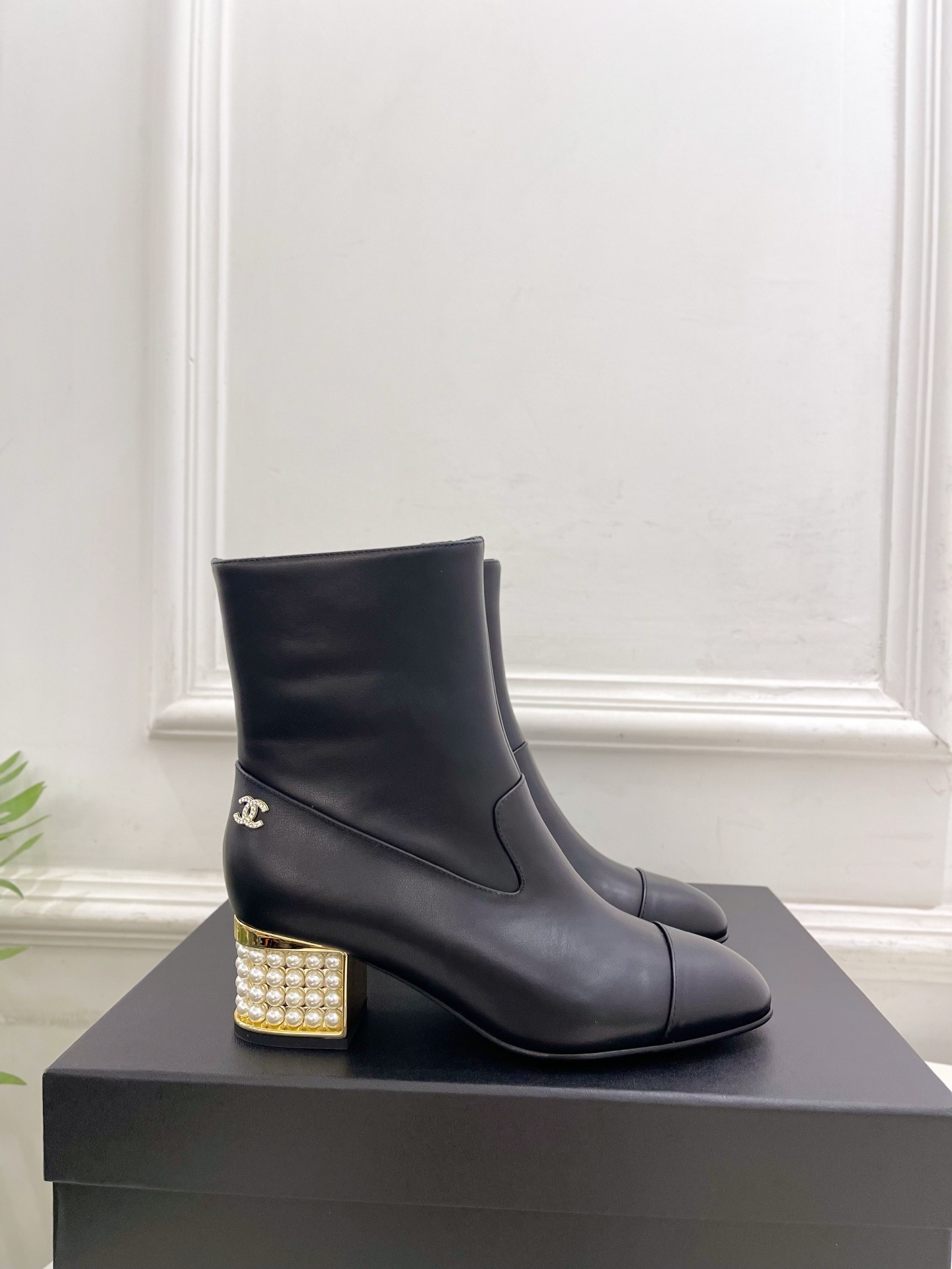 Elegant black leather ankle boots featuring a unique gold block heel decorated with rows of white pearls. - Hình 2