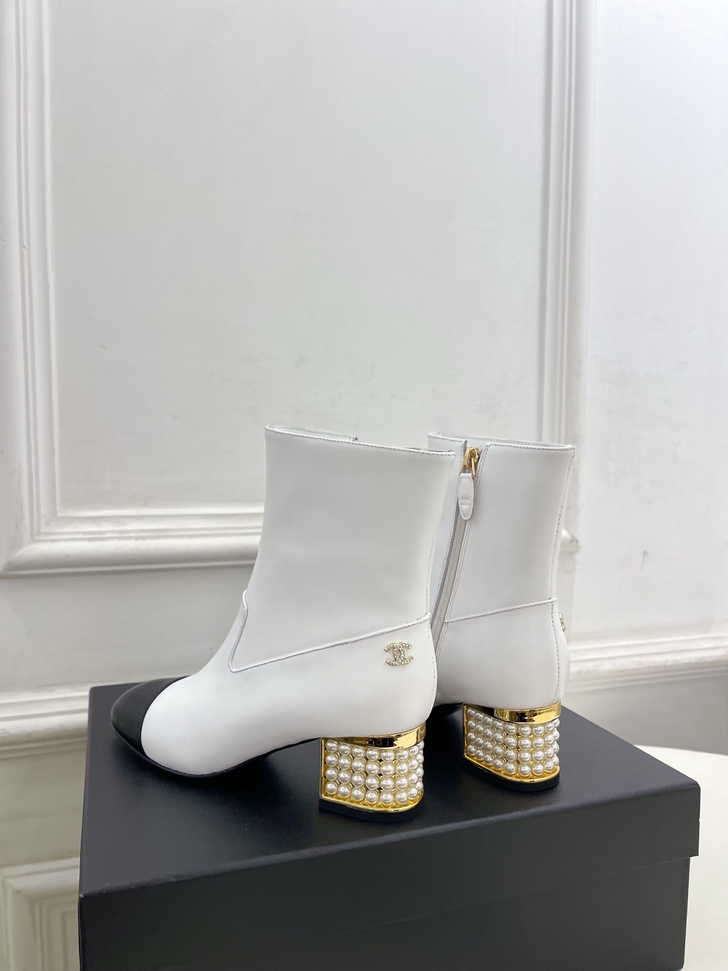 Luxury white leather ankle boots with black toe caps and gold pearl-encrusted block heels displayed on a black box. - Hình 8
