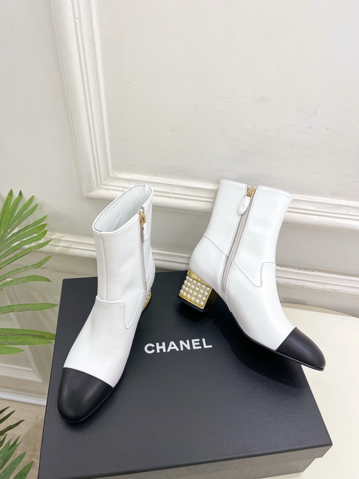Luxury white leather ankle boots with black toe caps and gold pearl-encrusted block heels displayed on a black box. - Hình 5