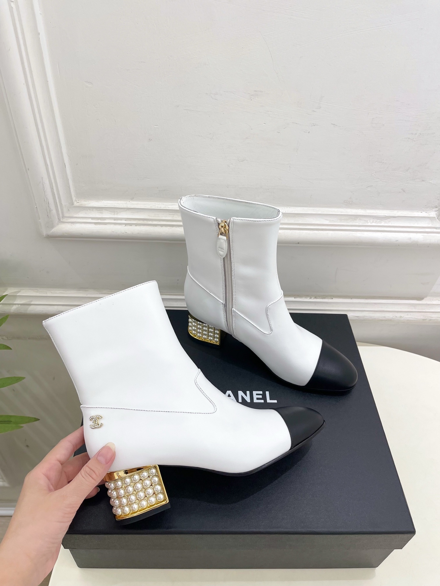 Luxury white leather ankle boots with black toe caps and gold pearl-encrusted block heels displayed on a black box. - Hình 4