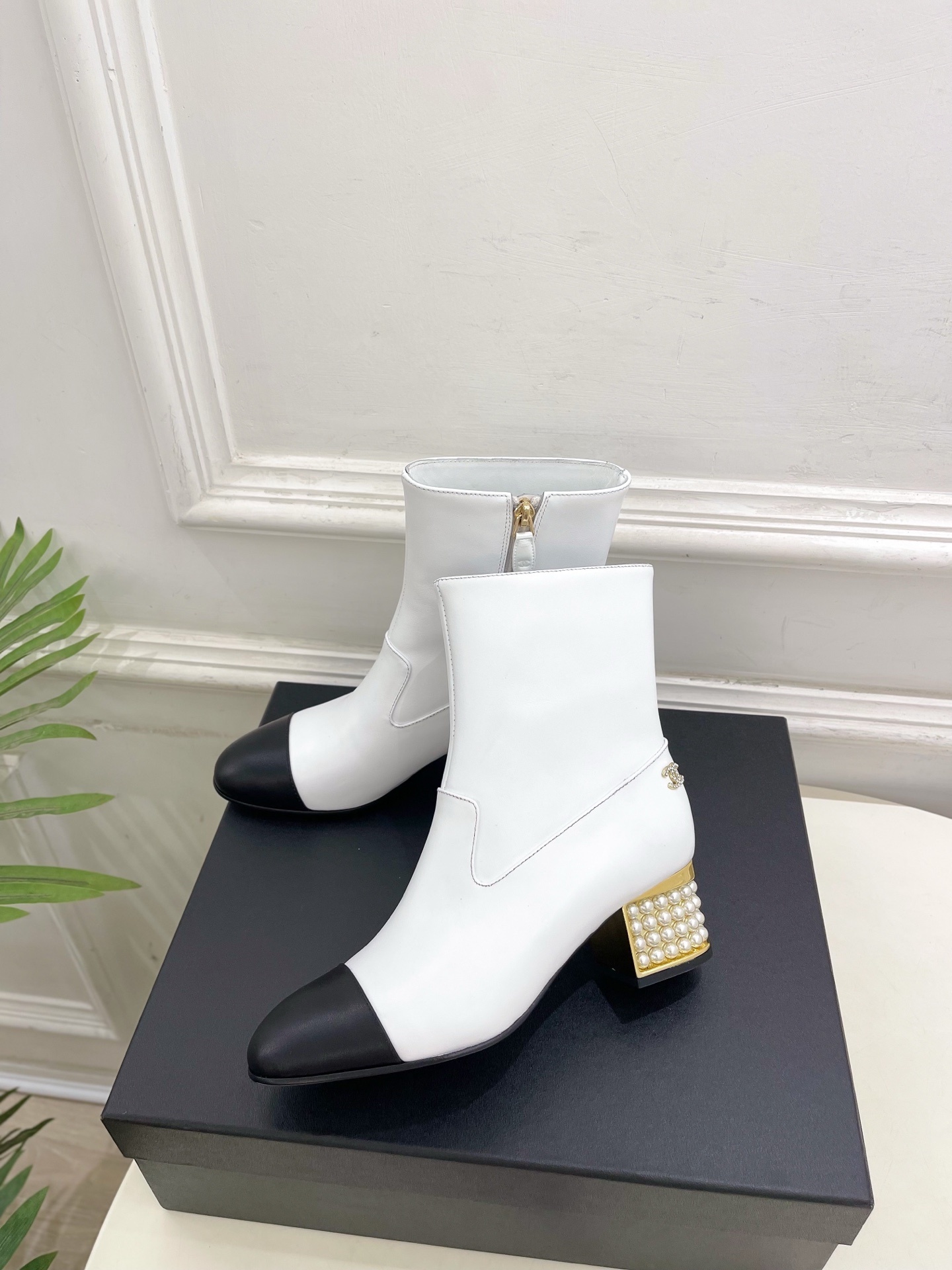 Luxury white leather ankle boots with black toe caps and gold pearl-encrusted block heels displayed on a black box. - Hình 3