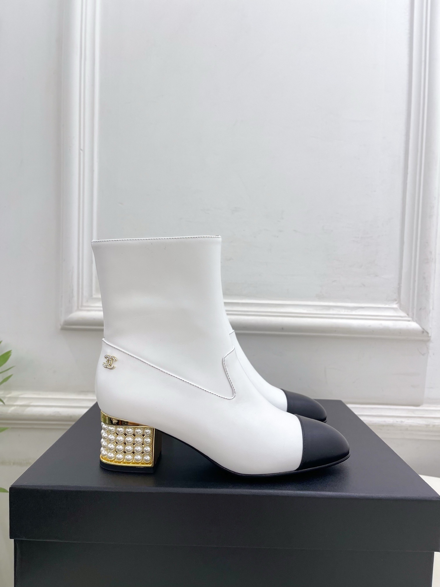 Luxury white leather ankle boots with black toe caps and gold pearl-encrusted block heels displayed on a black box. - Hình 2