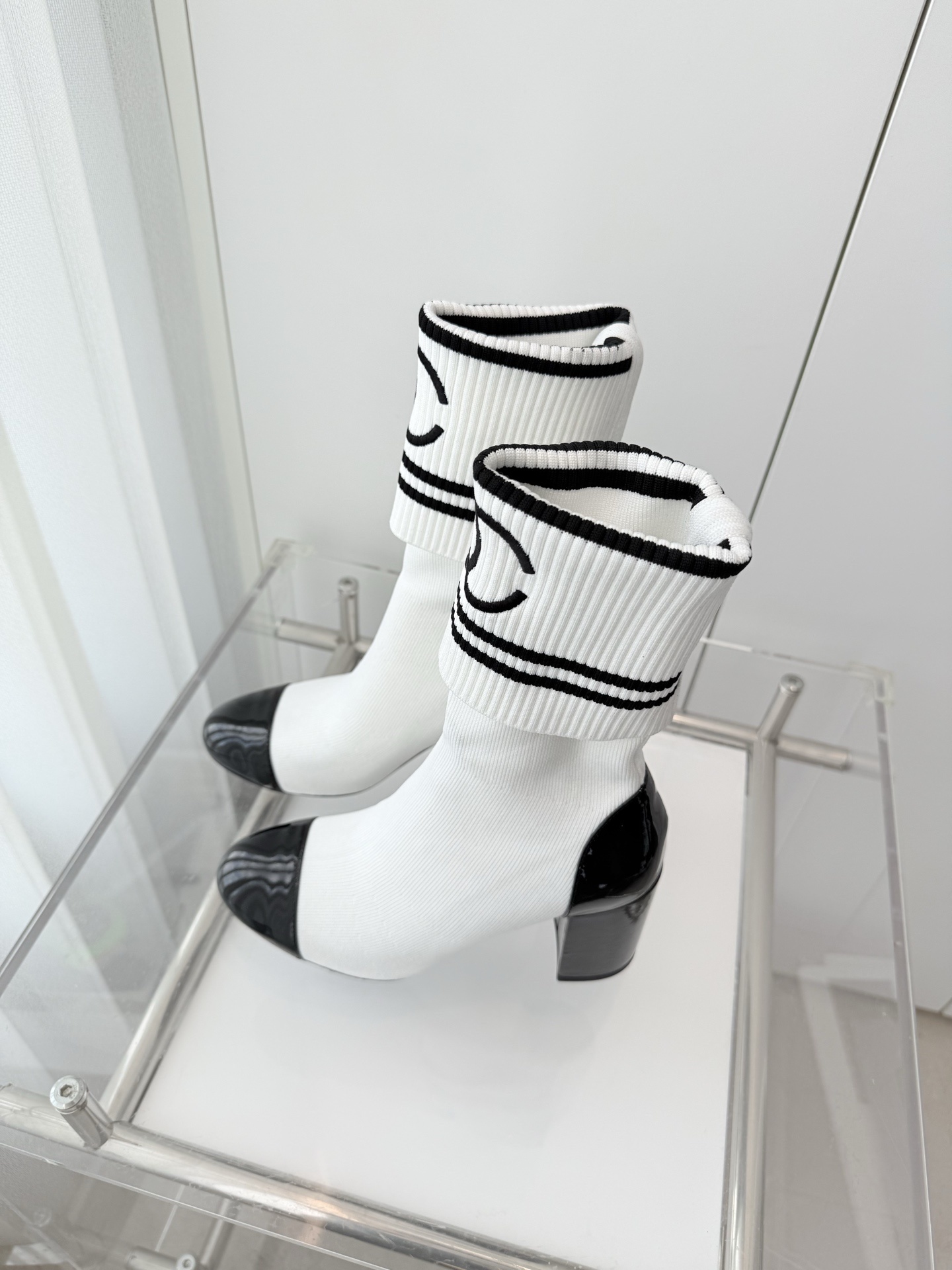 A pair of luxury white knit sock boots with black patent leather toe caps and block heels, featuring a black logo on the ribbed cuff. - Hình 9