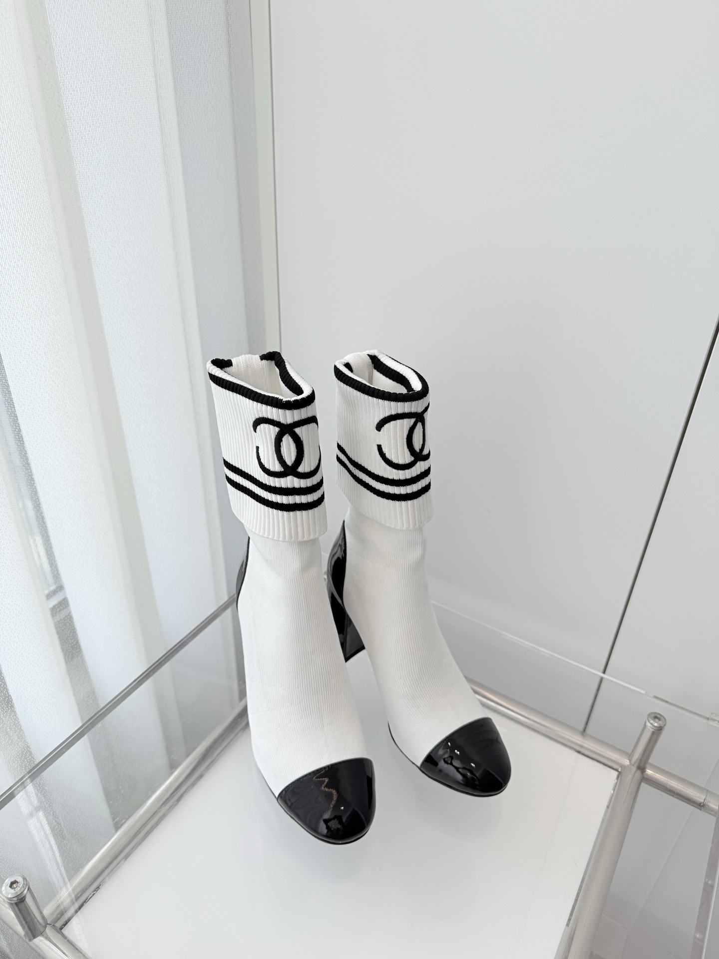 A pair of luxury white knit sock boots with black patent leather toe caps and block heels, featuring a black logo on the ribbed cuff. - Hình 8
