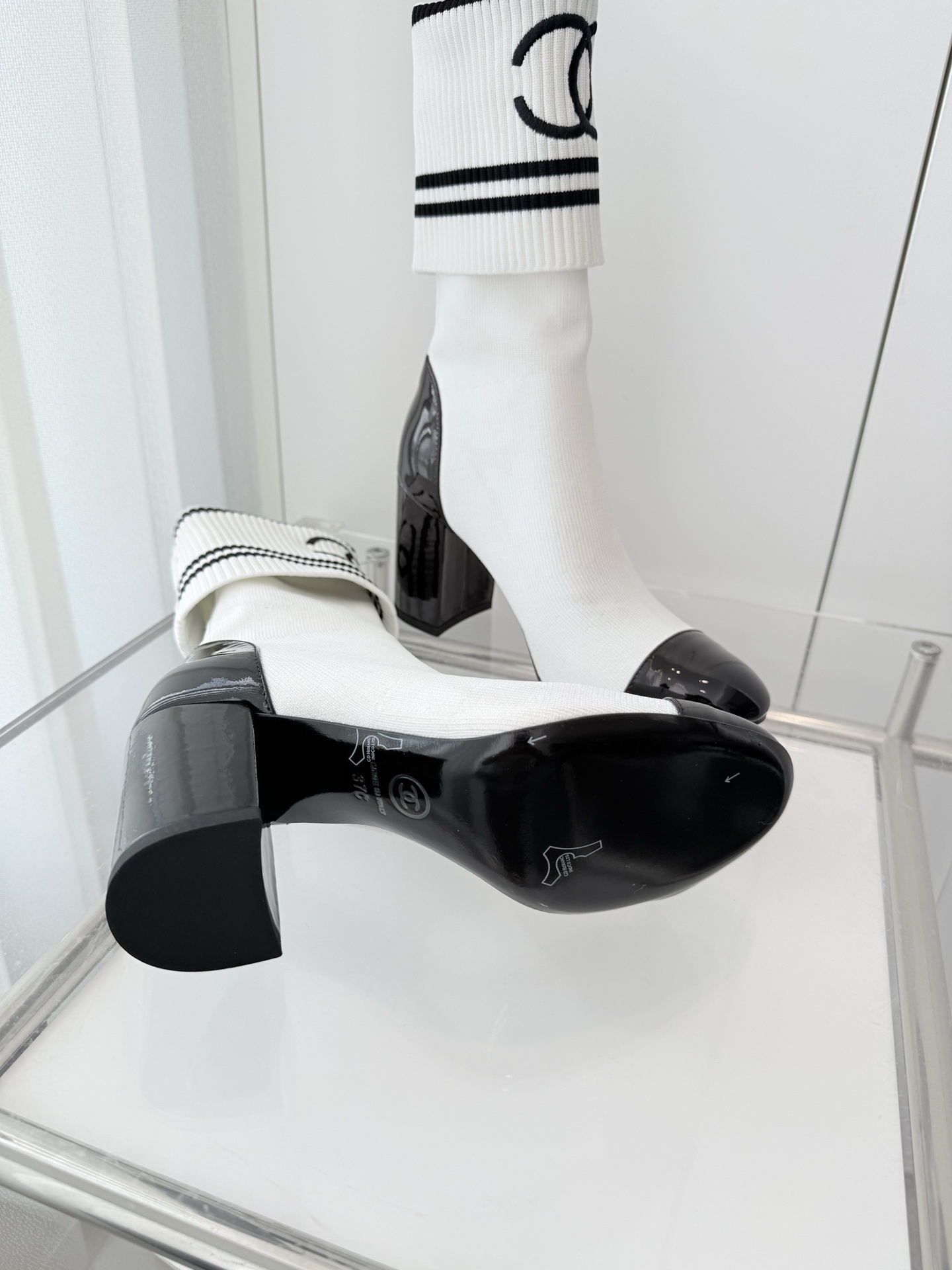 A pair of luxury white knit sock boots with black patent leather toe caps and block heels, featuring a black logo on the ribbed cuff. - Hình 7