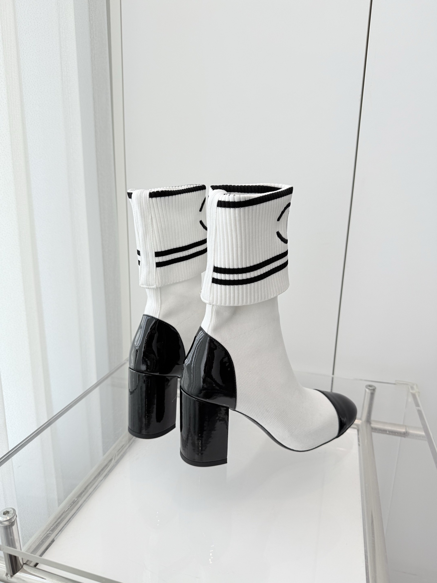 A pair of luxury white knit sock boots with black patent leather toe caps and block heels, featuring a black logo on the ribbed cuff. - Hình 6