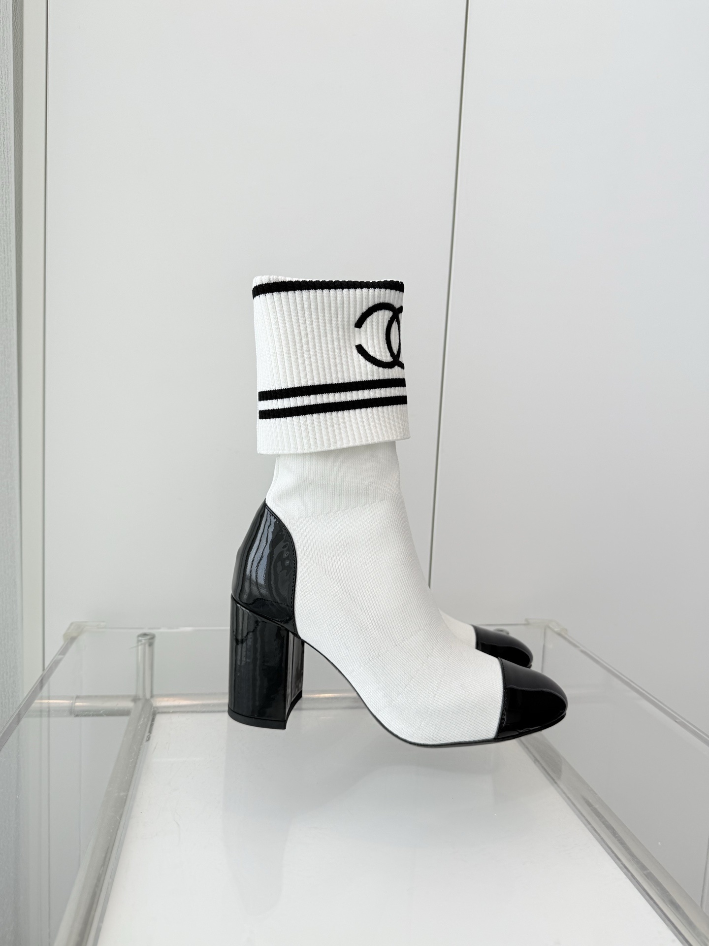 A pair of luxury white knit sock boots with black patent leather toe caps and block heels, featuring a black logo on the ribbed cuff. - Hình 5