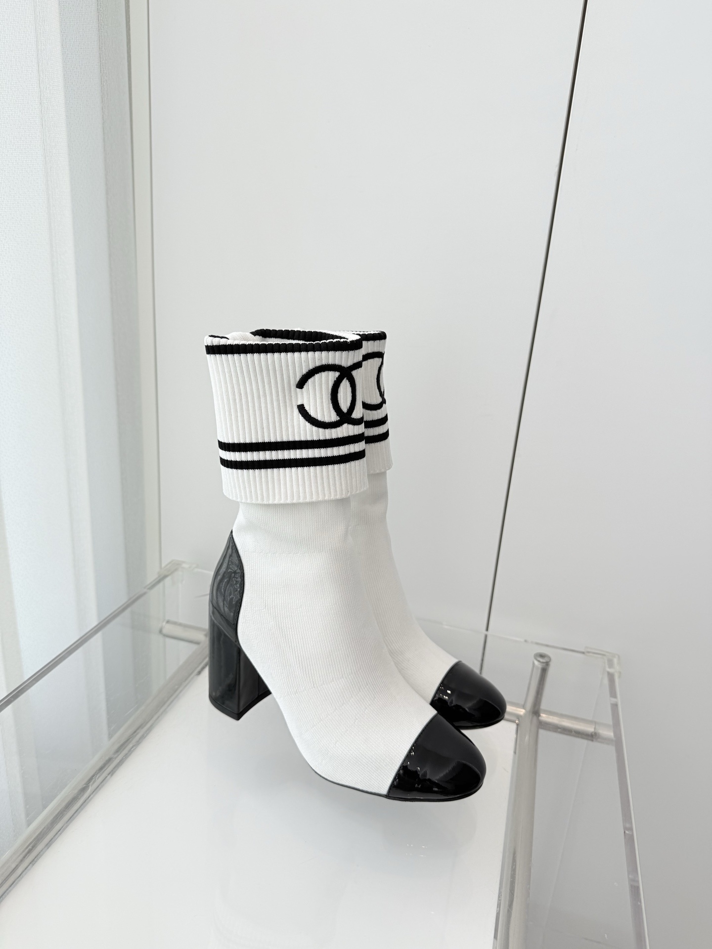 A pair of luxury white knit sock boots with black patent leather toe caps and block heels, featuring a black logo on the ribbed cuff. - Hình 4