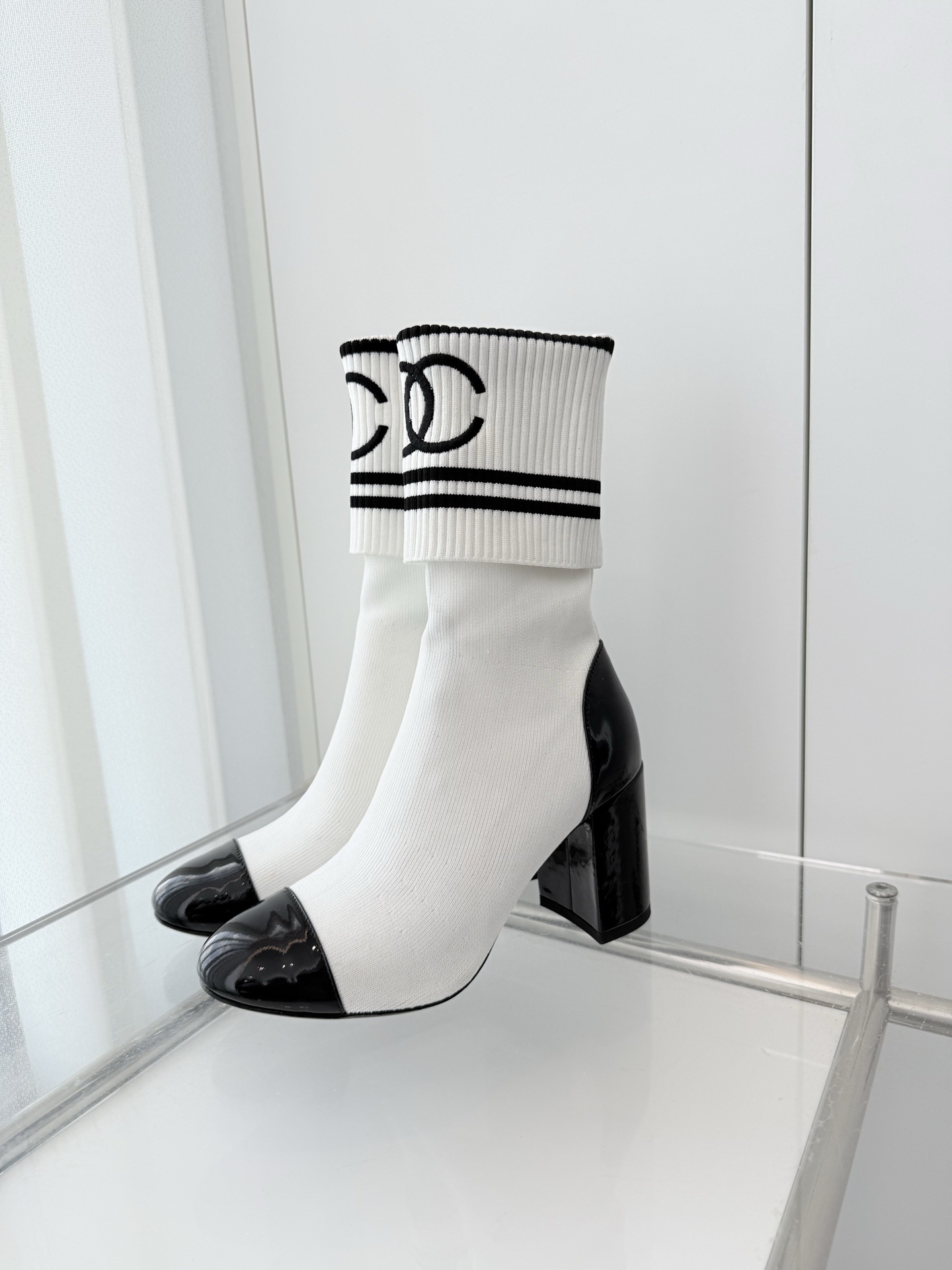 A pair of luxury white knit sock boots with black patent leather toe caps and block heels, featuring a black logo on the ribbed cuff. - Hình 3