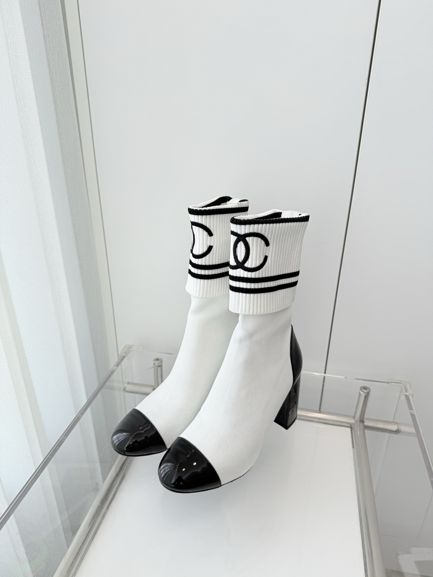 A pair of luxury white knit sock boots with black patent leather toe caps and block heels, featuring a black logo on the ribbed cuff. - Hình 2