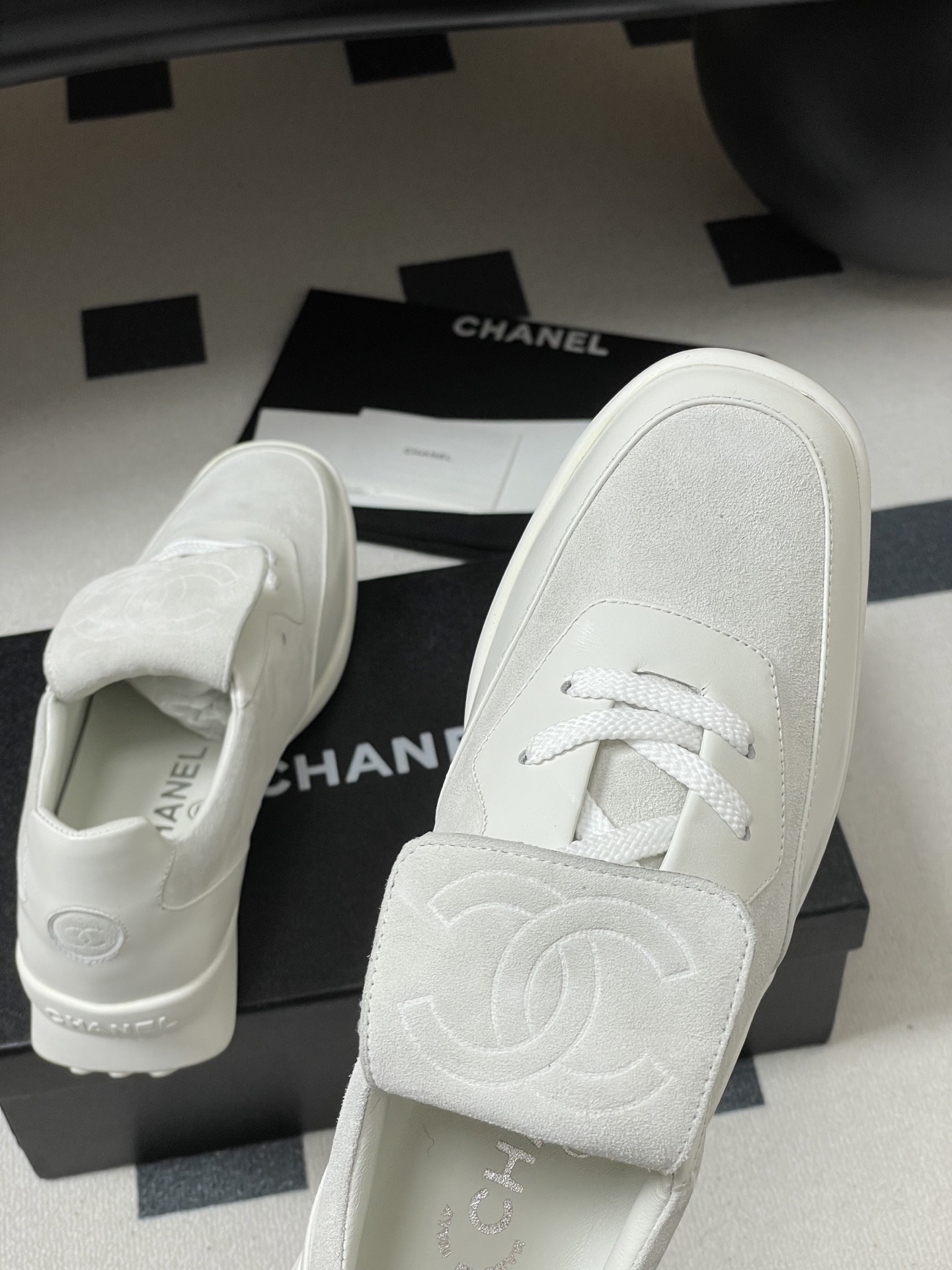 Pair of Chanel white leather and suede sneakers with embossed CC logo flap on a black surface - Hình 9