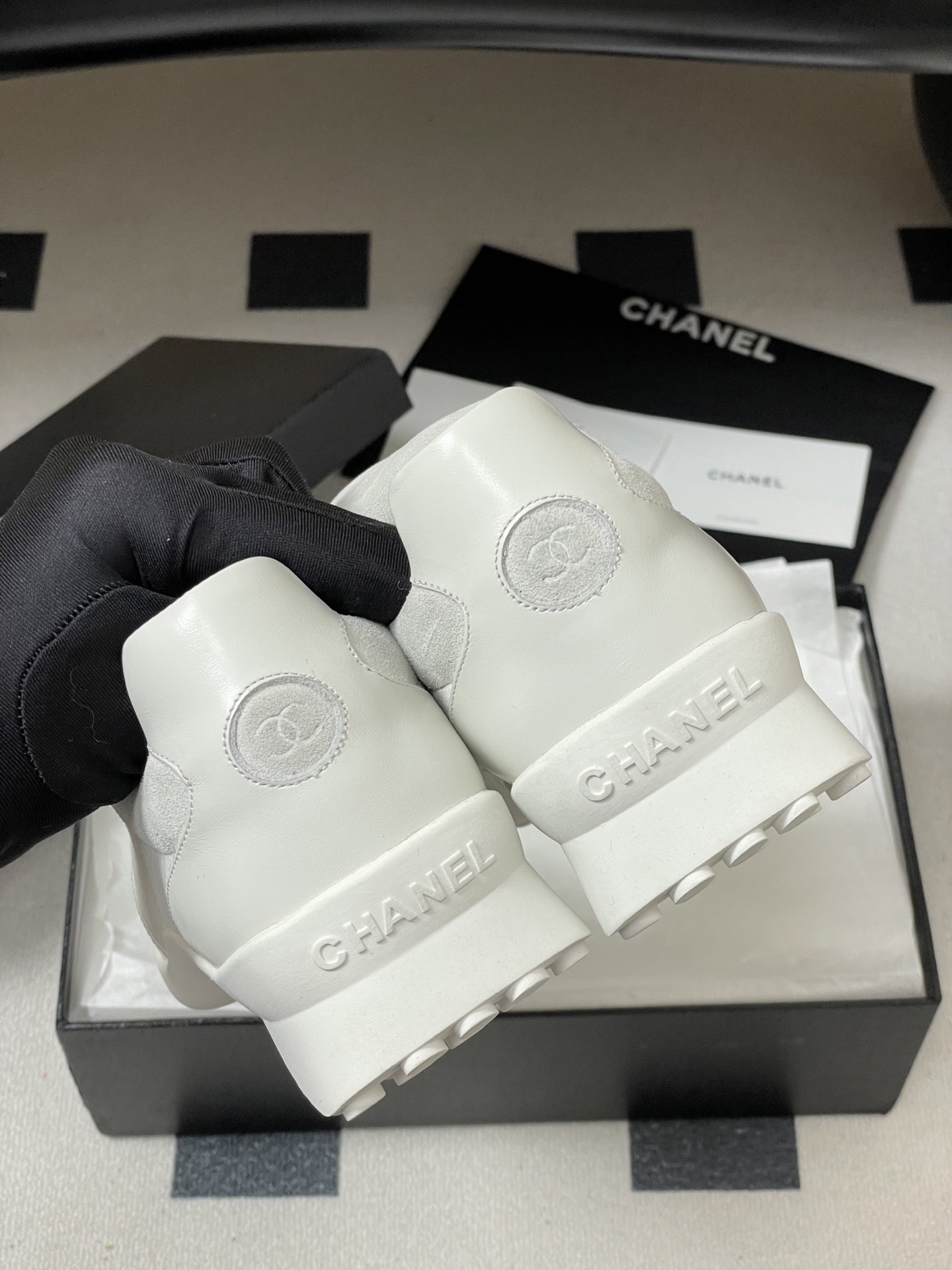 Pair of Chanel white leather and suede sneakers with embossed CC logo flap on a black surface - Hình 7