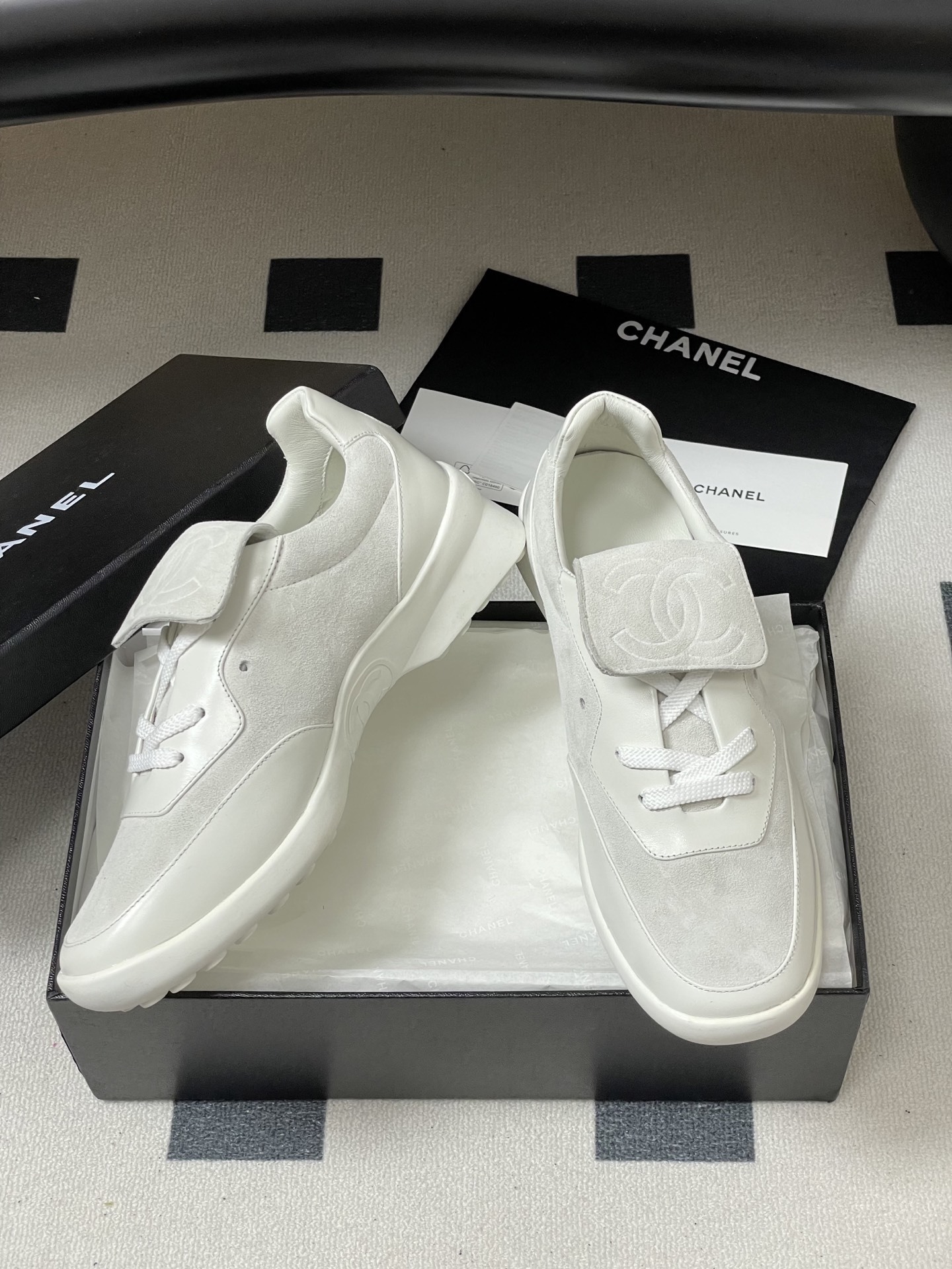 Pair of Chanel white leather and suede sneakers with embossed CC logo flap on a black surface - Hình 5