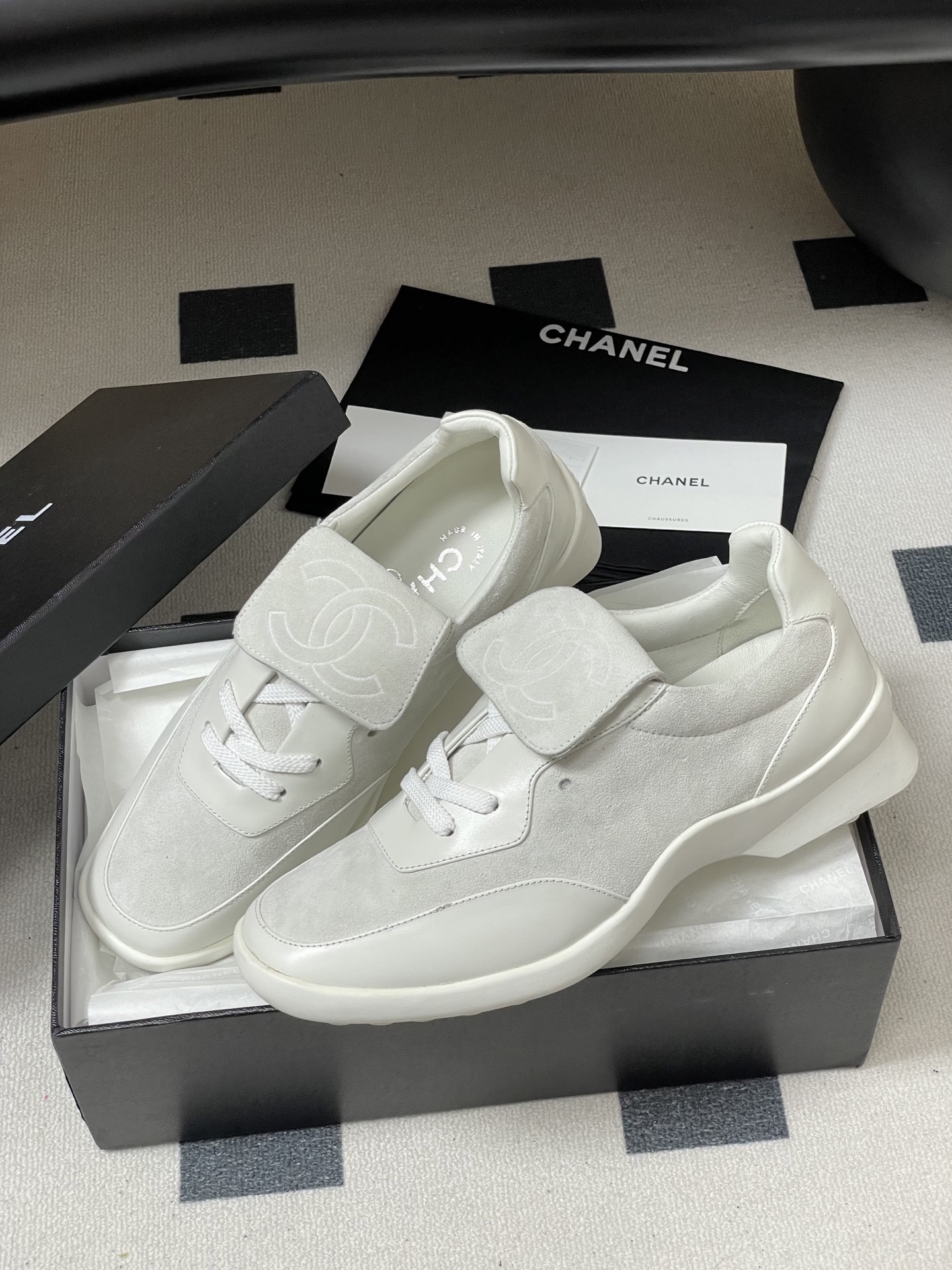 Pair of Chanel white leather and suede sneakers with embossed CC logo flap on a black surface - Hình 4