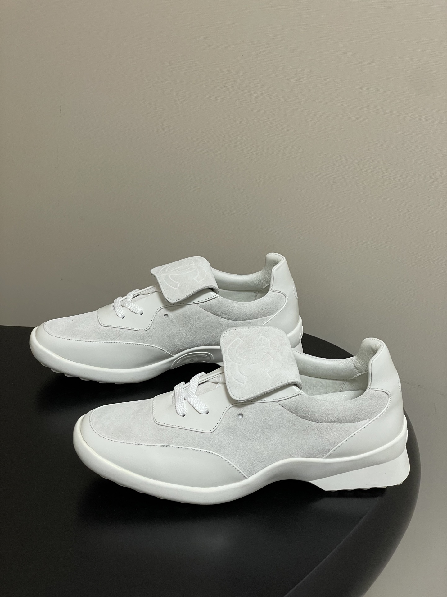 Pair of Chanel white leather and suede sneakers with embossed CC logo flap on a black surface - Hình 3