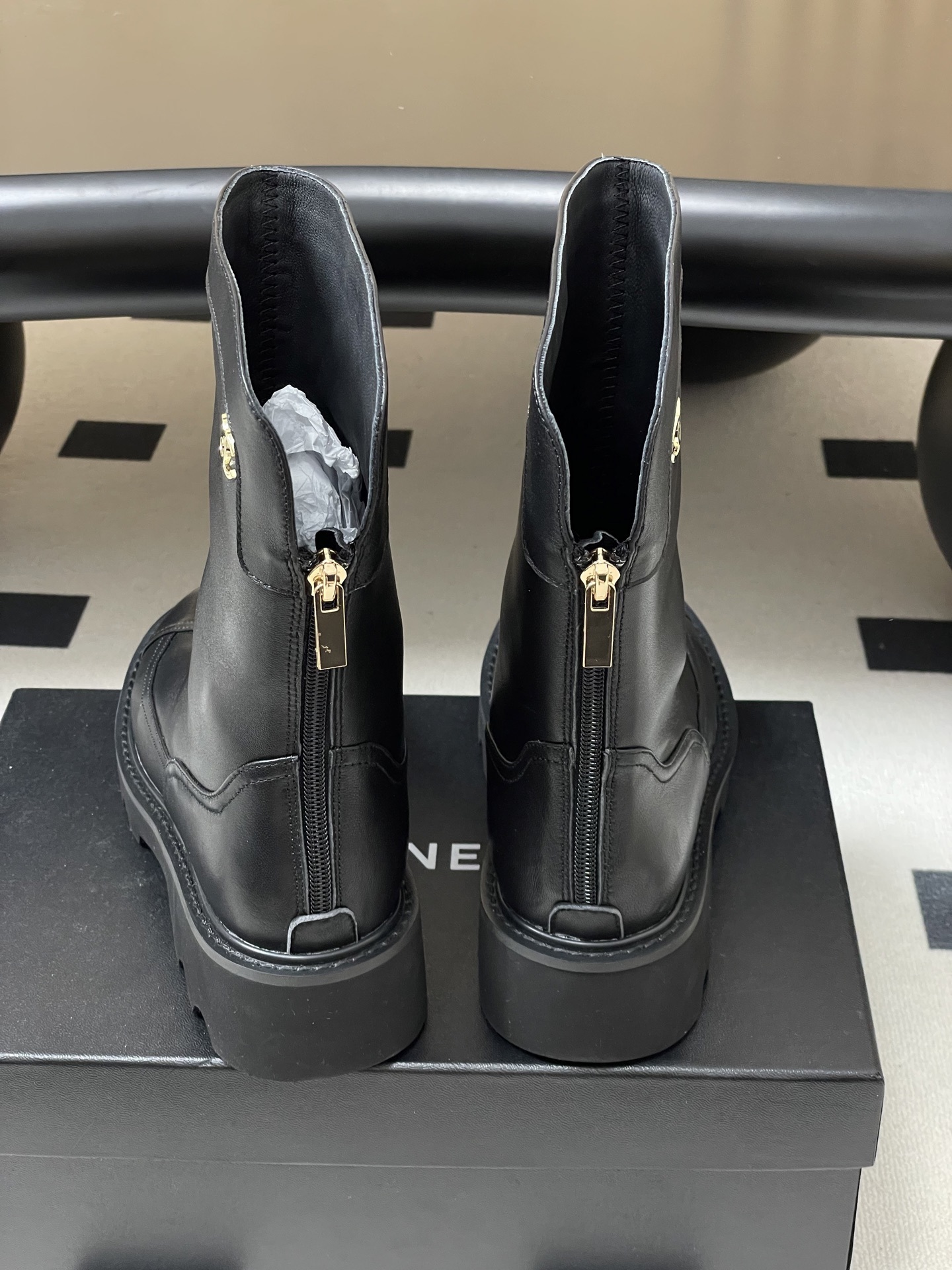 Pair of Chanel black leather mid-calf boots with chunky lug soles and gold CC logo hardware on a black surface. - Hình 9