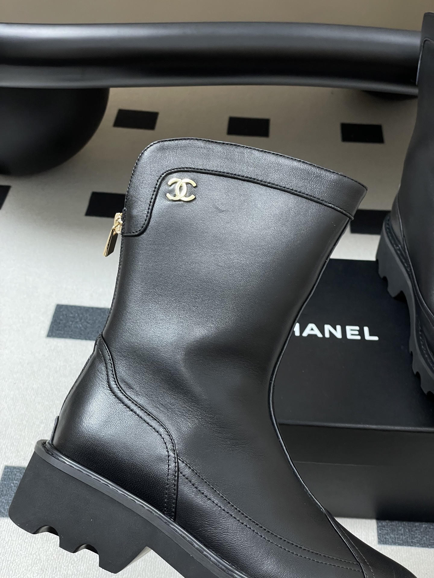 Pair of Chanel black leather mid-calf boots with chunky lug soles and gold CC logo hardware on a black surface. - Hình 8