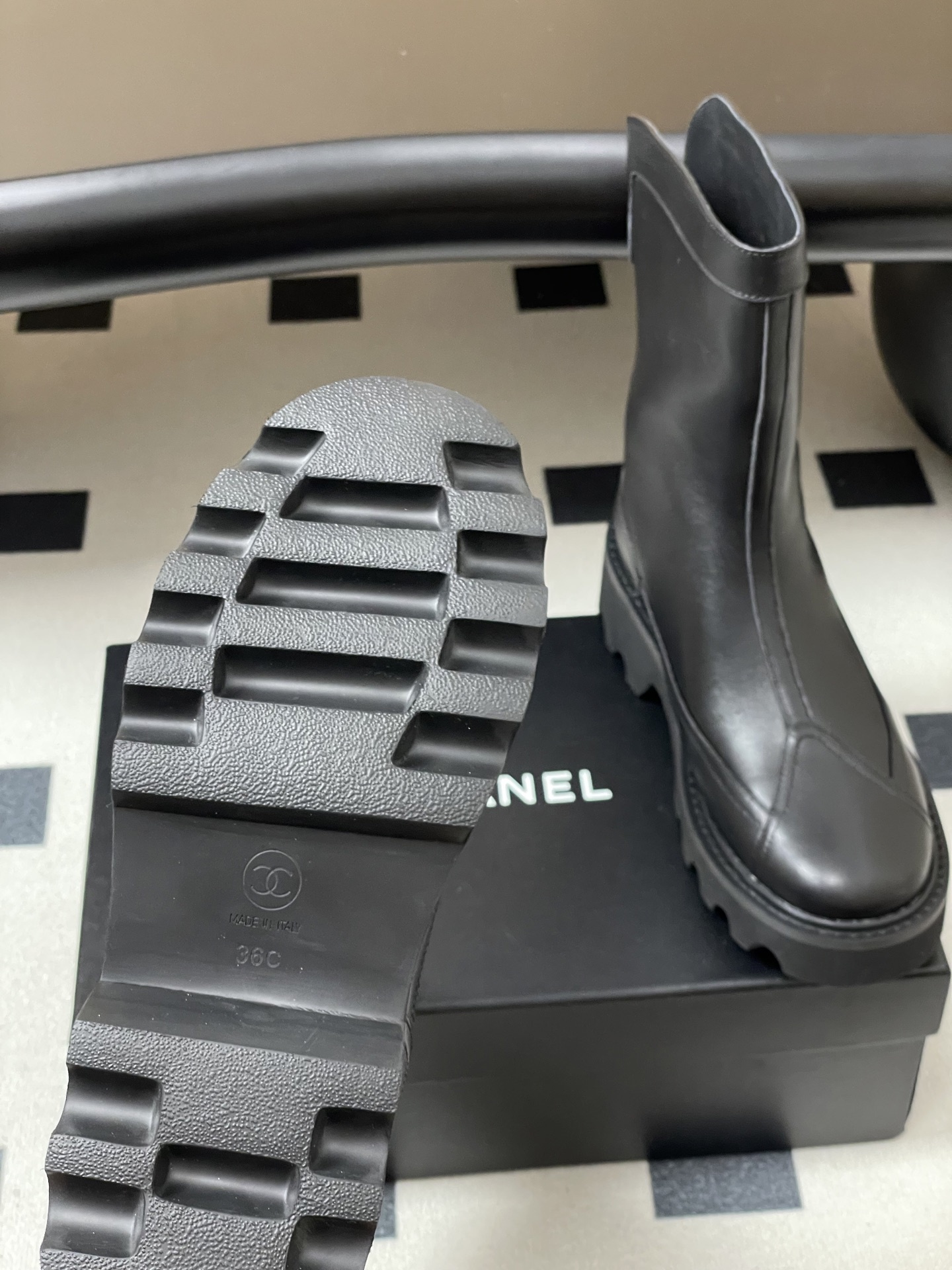 Pair of Chanel black leather mid-calf boots with chunky lug soles and gold CC logo hardware on a black surface. - Hình 7