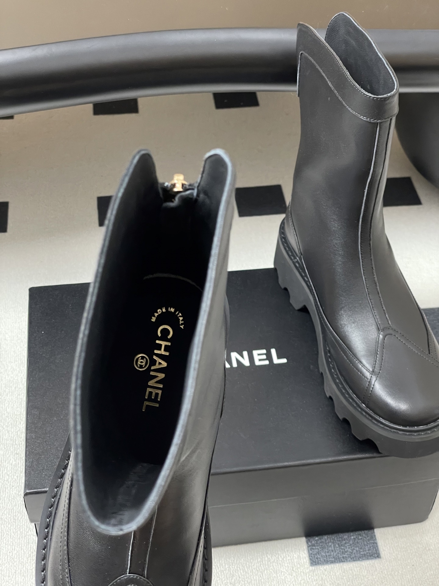Pair of Chanel black leather mid-calf boots with chunky lug soles and gold CC logo hardware on a black surface. - Hình 6