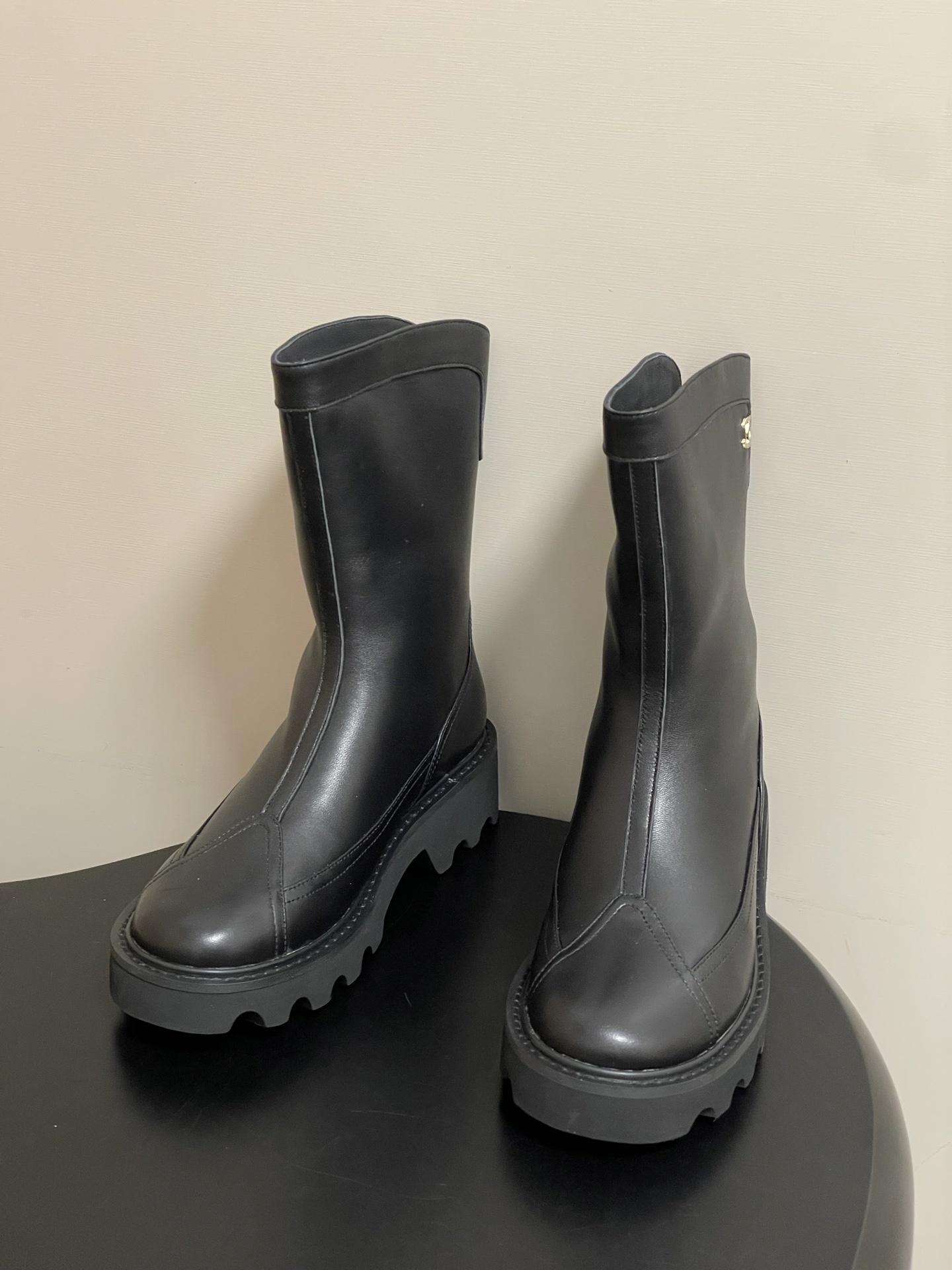 Pair of Chanel black leather mid-calf boots with chunky lug soles and gold CC logo hardware on a black surface. - Hình 2