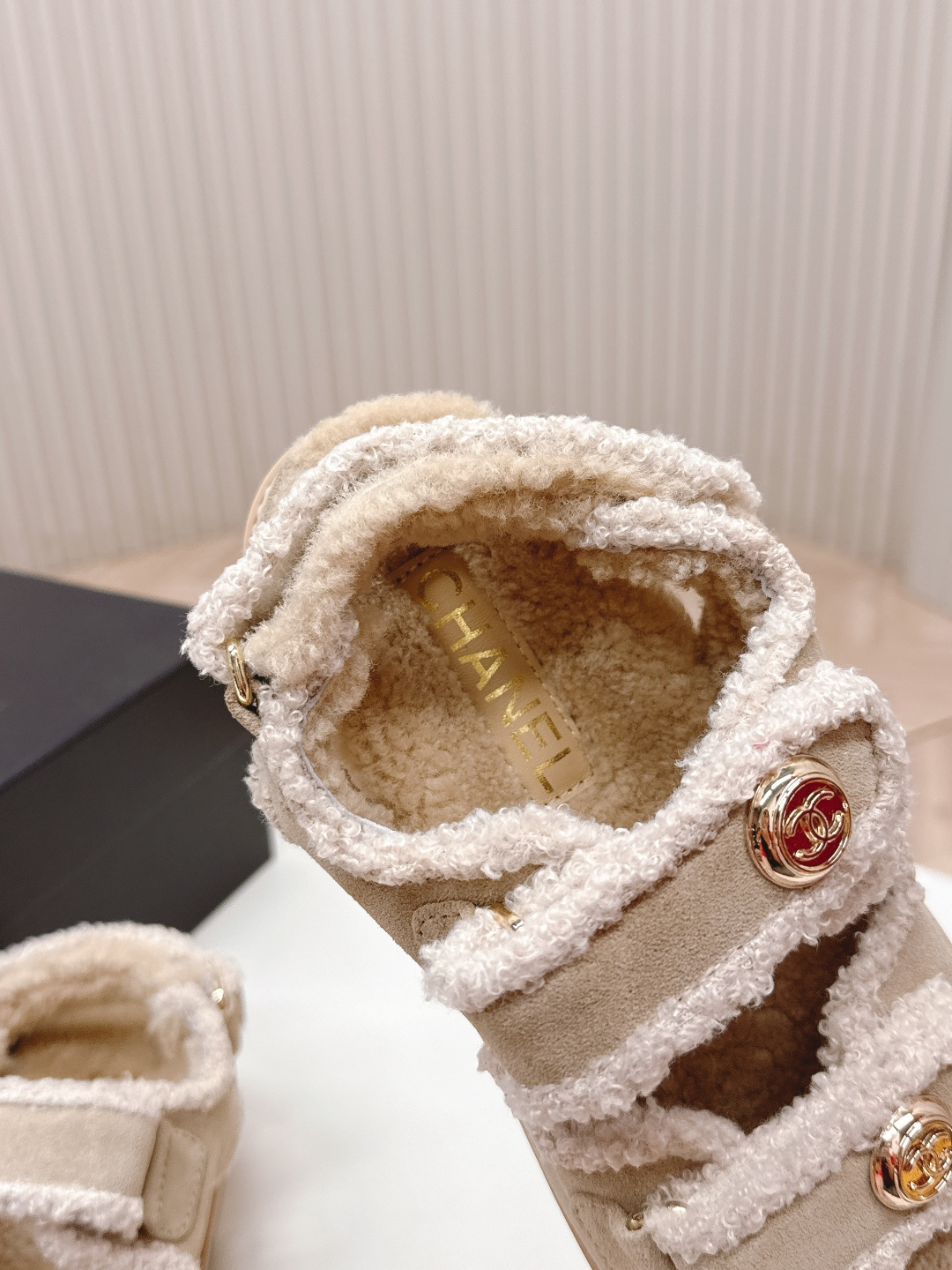 A pair of Chanel beige shearling dad sandals with gold CC logo buttons next to a black Chanel box. - Hình 5