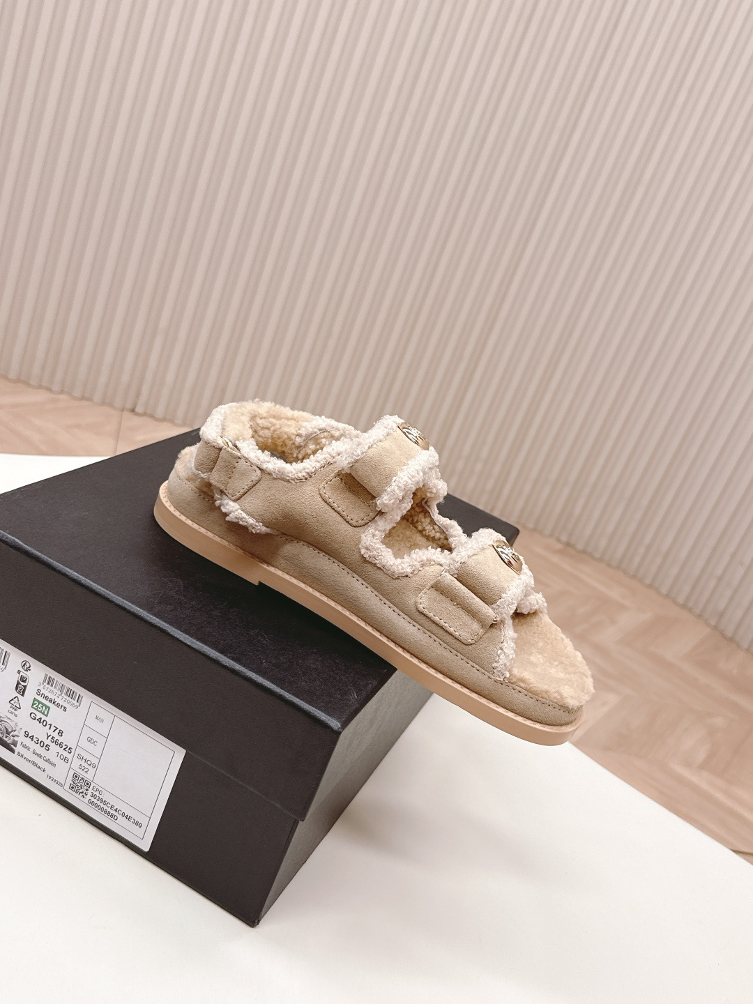 A pair of Chanel beige shearling dad sandals with gold CC logo buttons next to a black Chanel box. - Hình 4