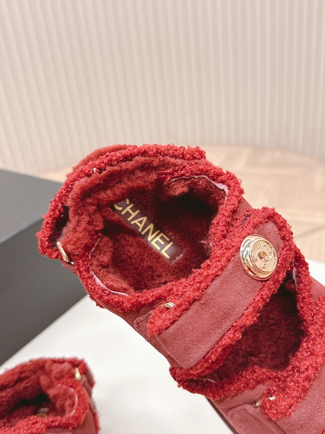 Luxury burgundy shearling sandals with gold logo buttons displayed on a white surface next to a brand box. - Hình 9