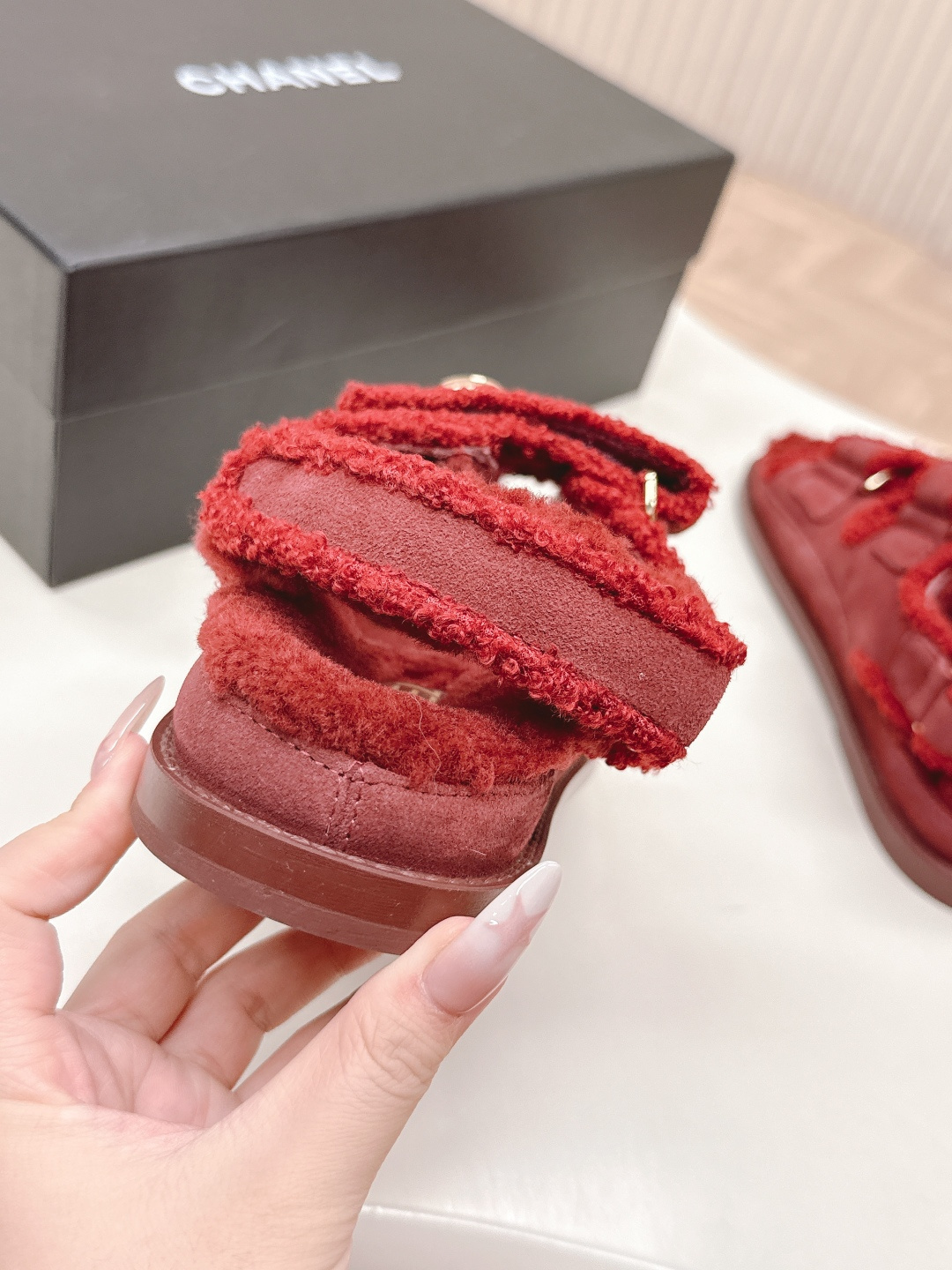 Luxury burgundy shearling sandals with gold logo buttons displayed on a white surface next to a brand box. - Hình 8