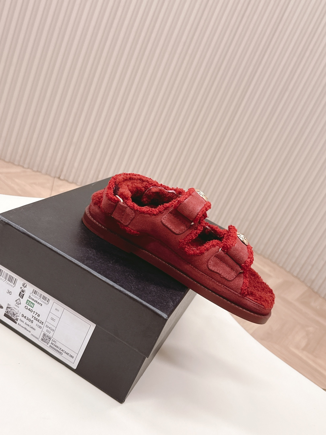 Luxury burgundy shearling sandals with gold logo buttons displayed on a white surface next to a brand box. - Hình 7