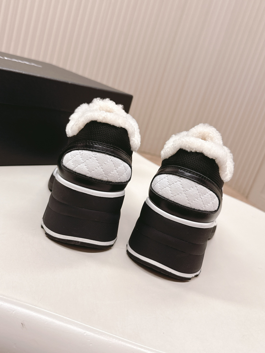 Pair of black Chanel sneakers with white shearling lining and chunky block heels on a white table - Hình 9