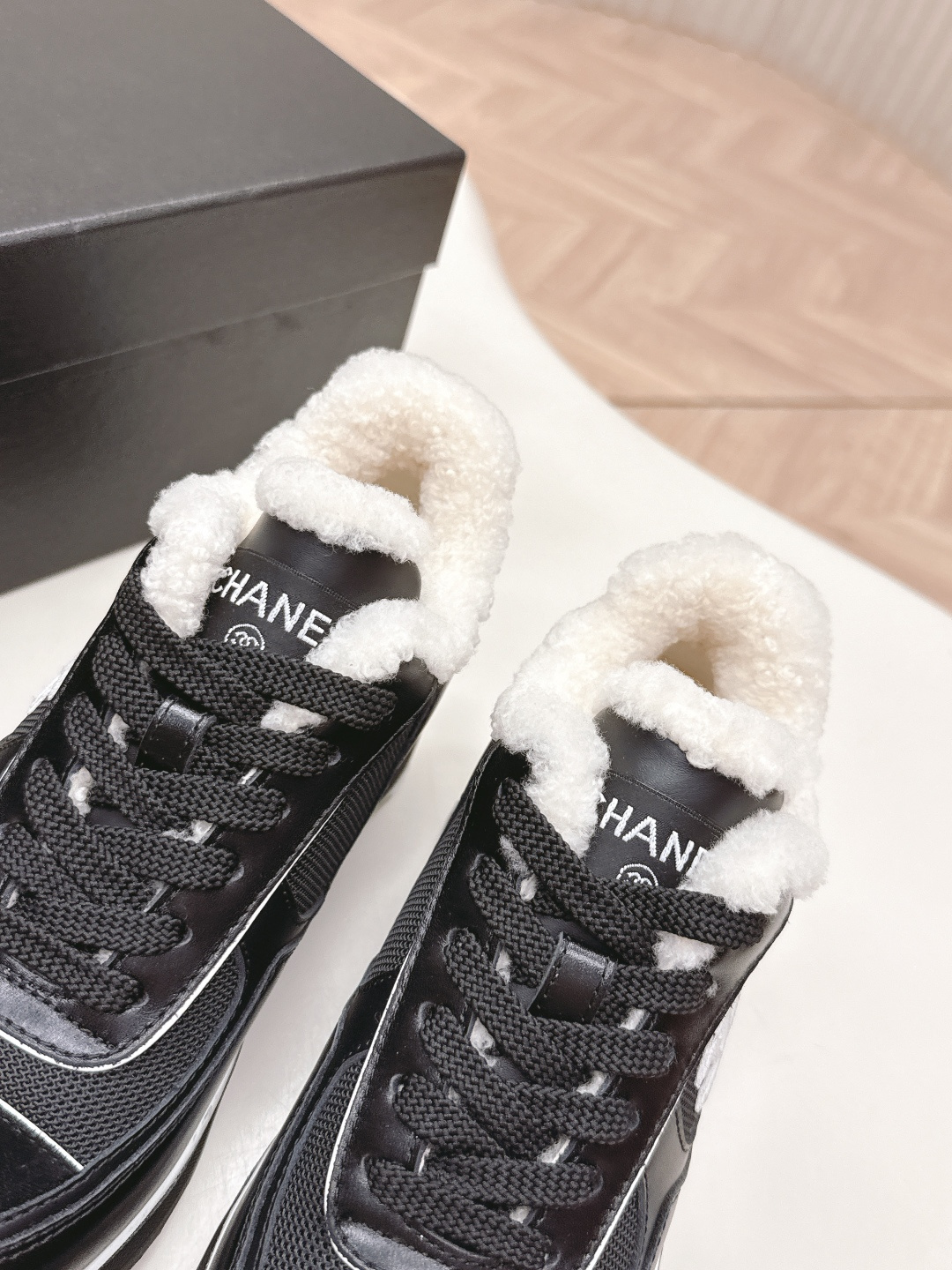 Pair of black Chanel sneakers with white shearling lining and chunky block heels on a white table - Hình 7