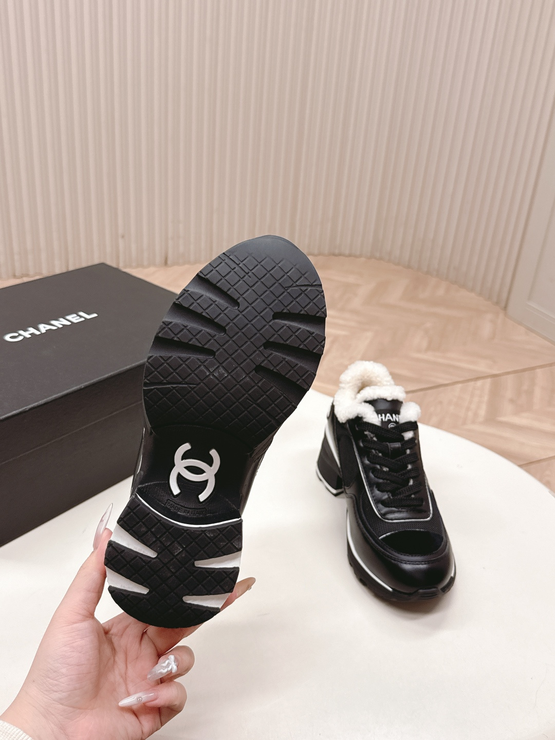 Pair of black Chanel sneakers with white shearling lining and chunky block heels on a white table - Hình 5
